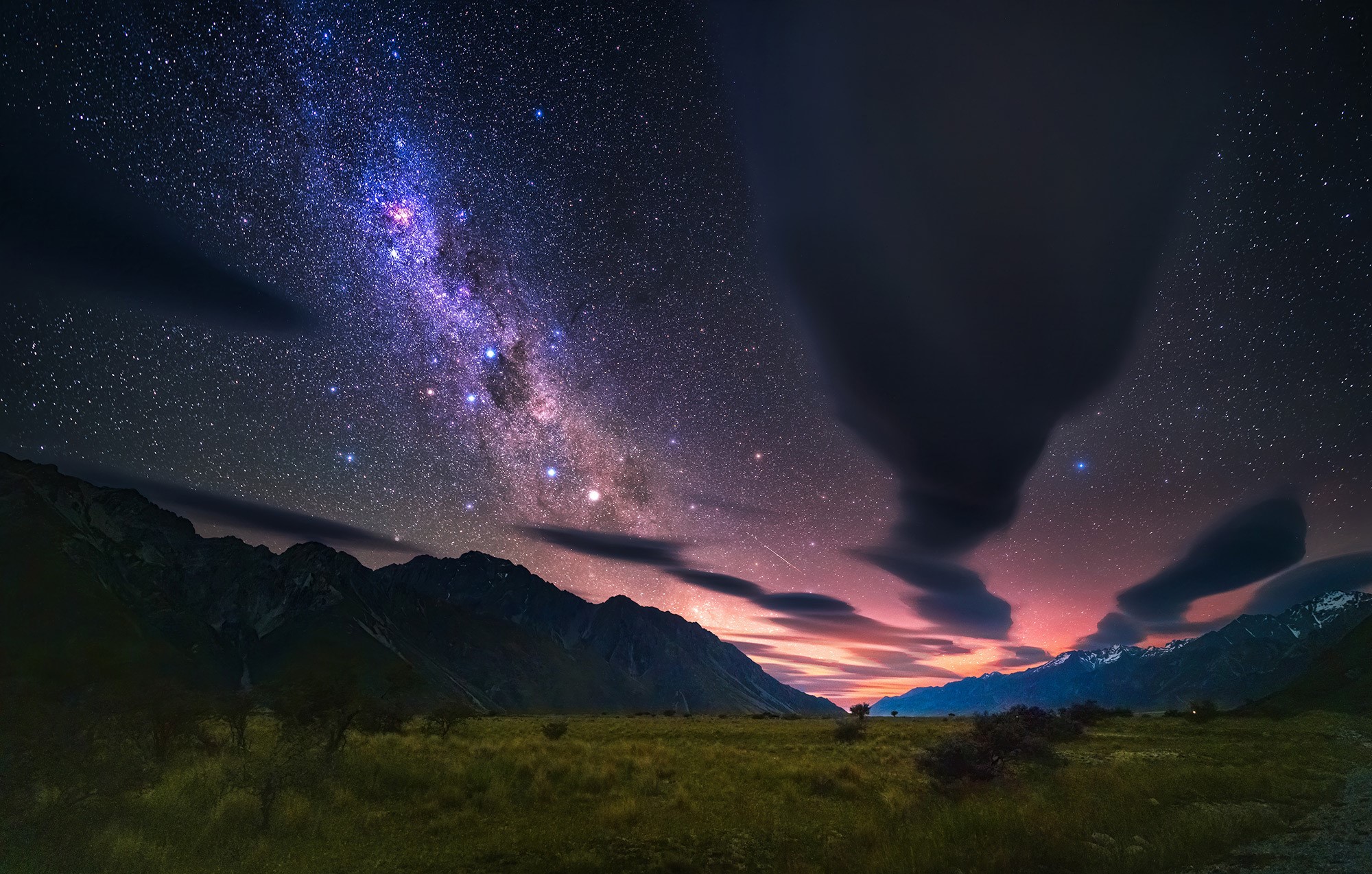 Milky Way over mountains and grassy field at night HD Wallpaper