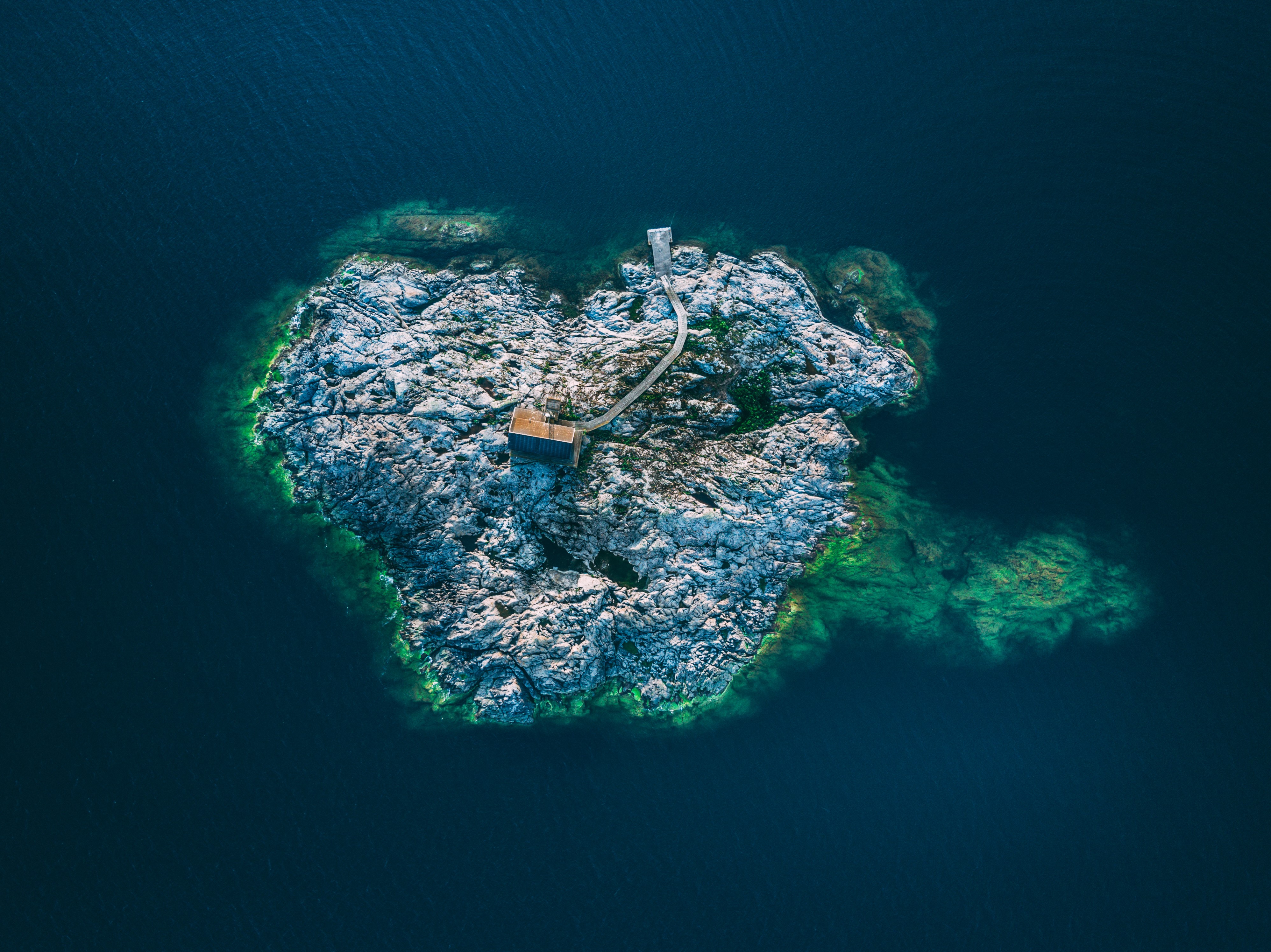 4K Aerial View of a Rocky Island with a Small Building HD Wallpaper