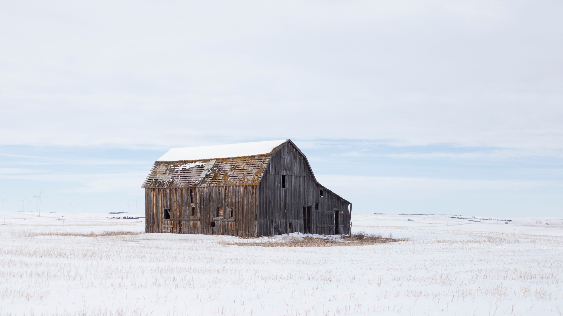 Abandoned barn in a snowy field with windmills HD Wallpaper