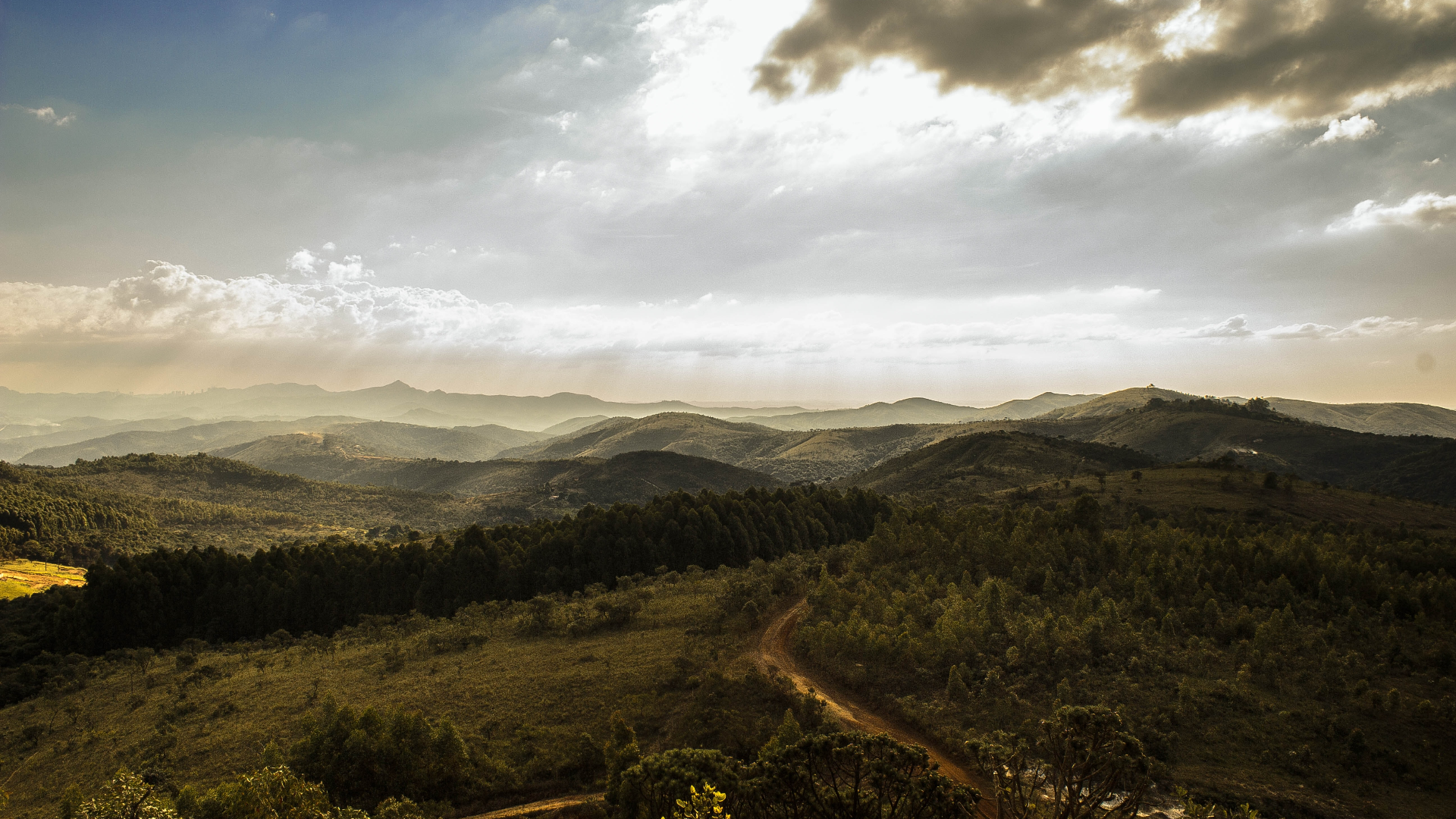 Rolling Hills and Mountains Under a Cloudy Sky HD Wallpaper