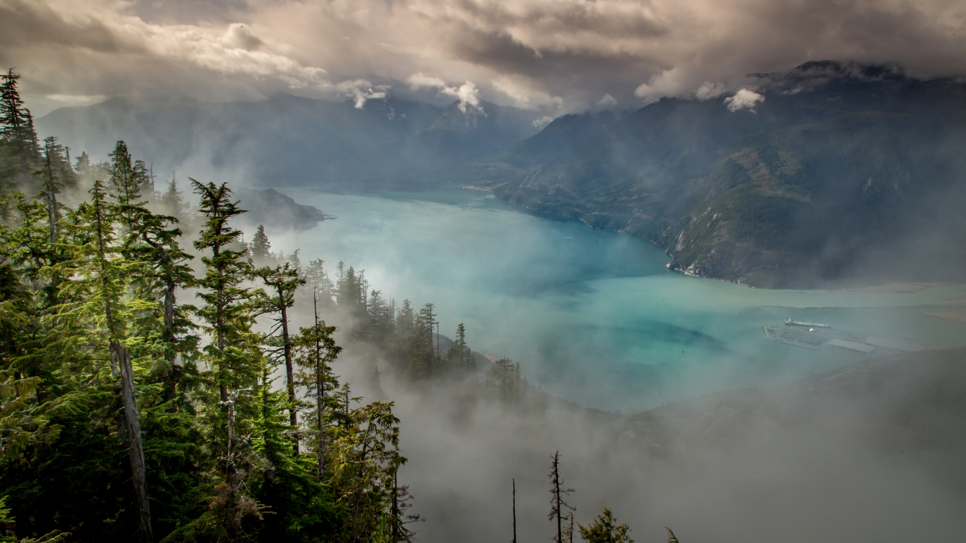 Misty mountains and turquoise lake with evergreen trees HD Wallpaper