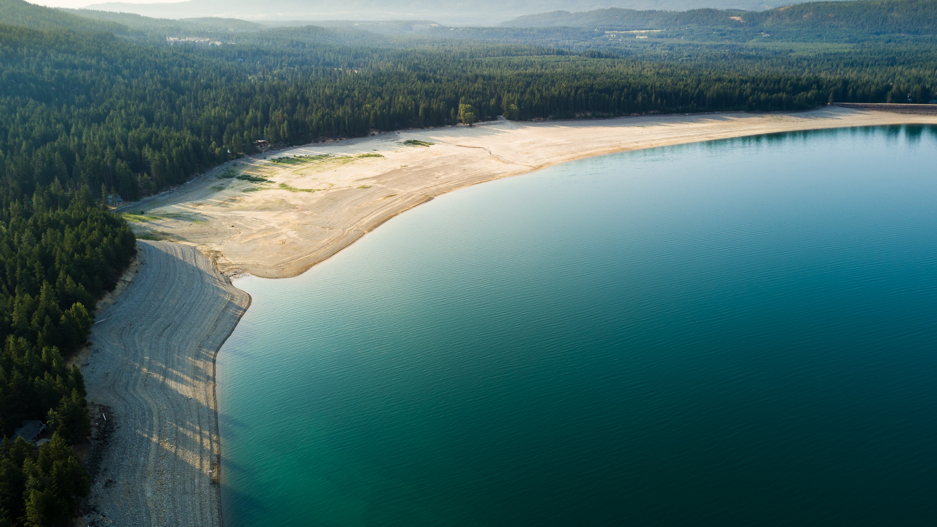 Aerial view of a lake shore with forest and mountains HD Wallpaper