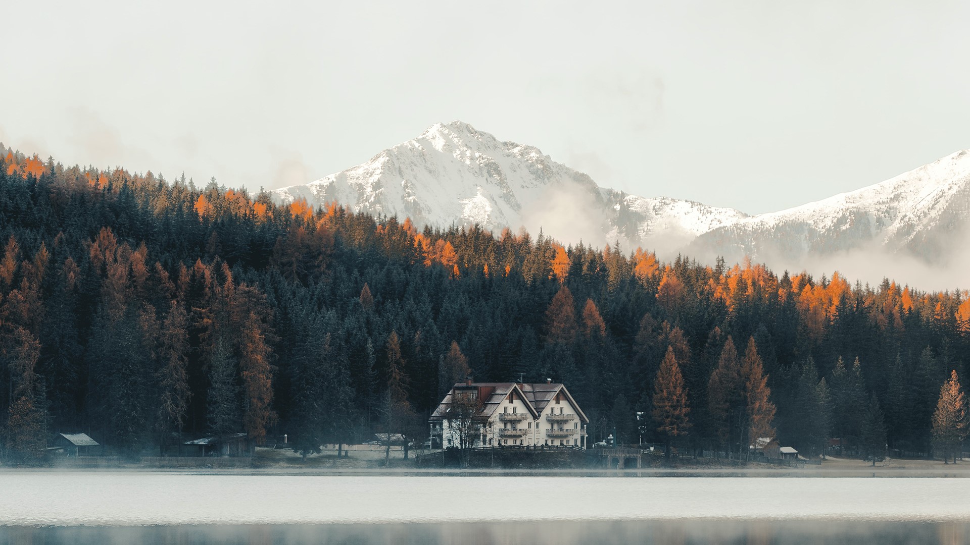 House by a lake with autumn forest and snowy mountains HD Wallpaper