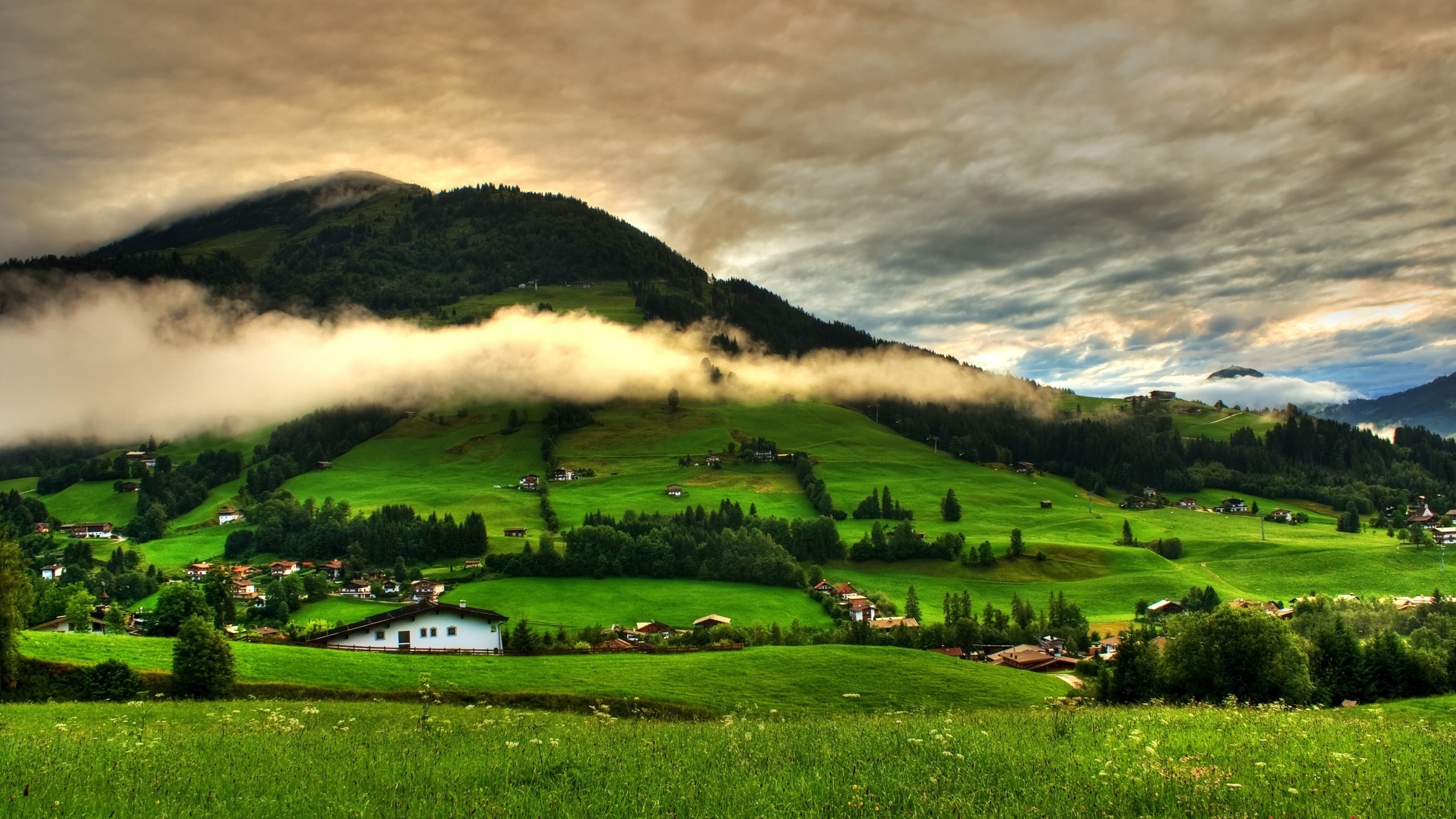 Green rolling hills with clouds over mountains HD Wallpaper