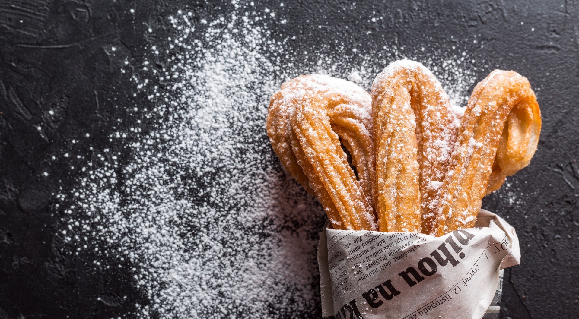 Churros dusted with powdered sugar on a dark surface HD Wallpaper