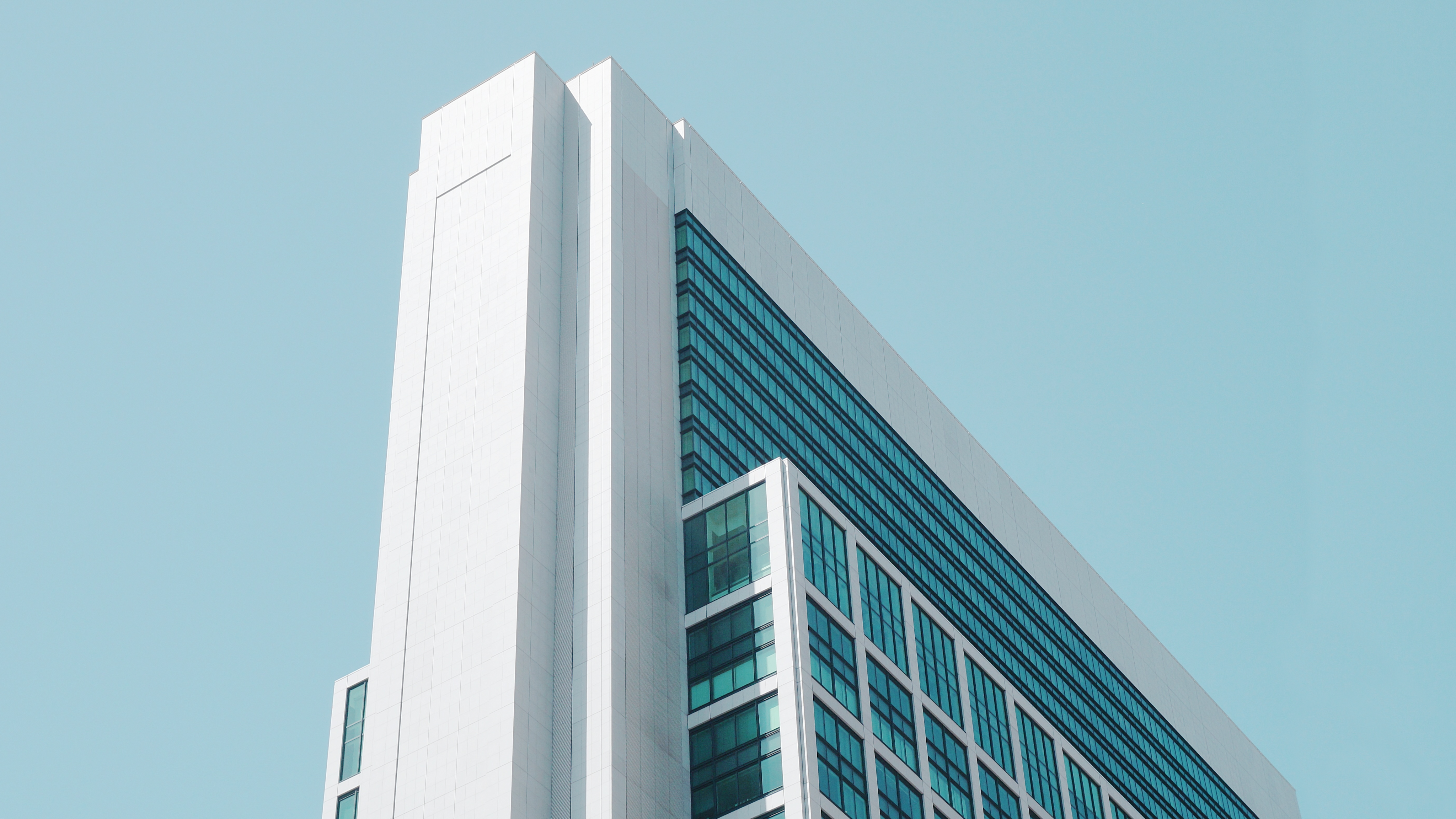 Modern white building with blue glass windows against a cyan sky HD Wallpaper