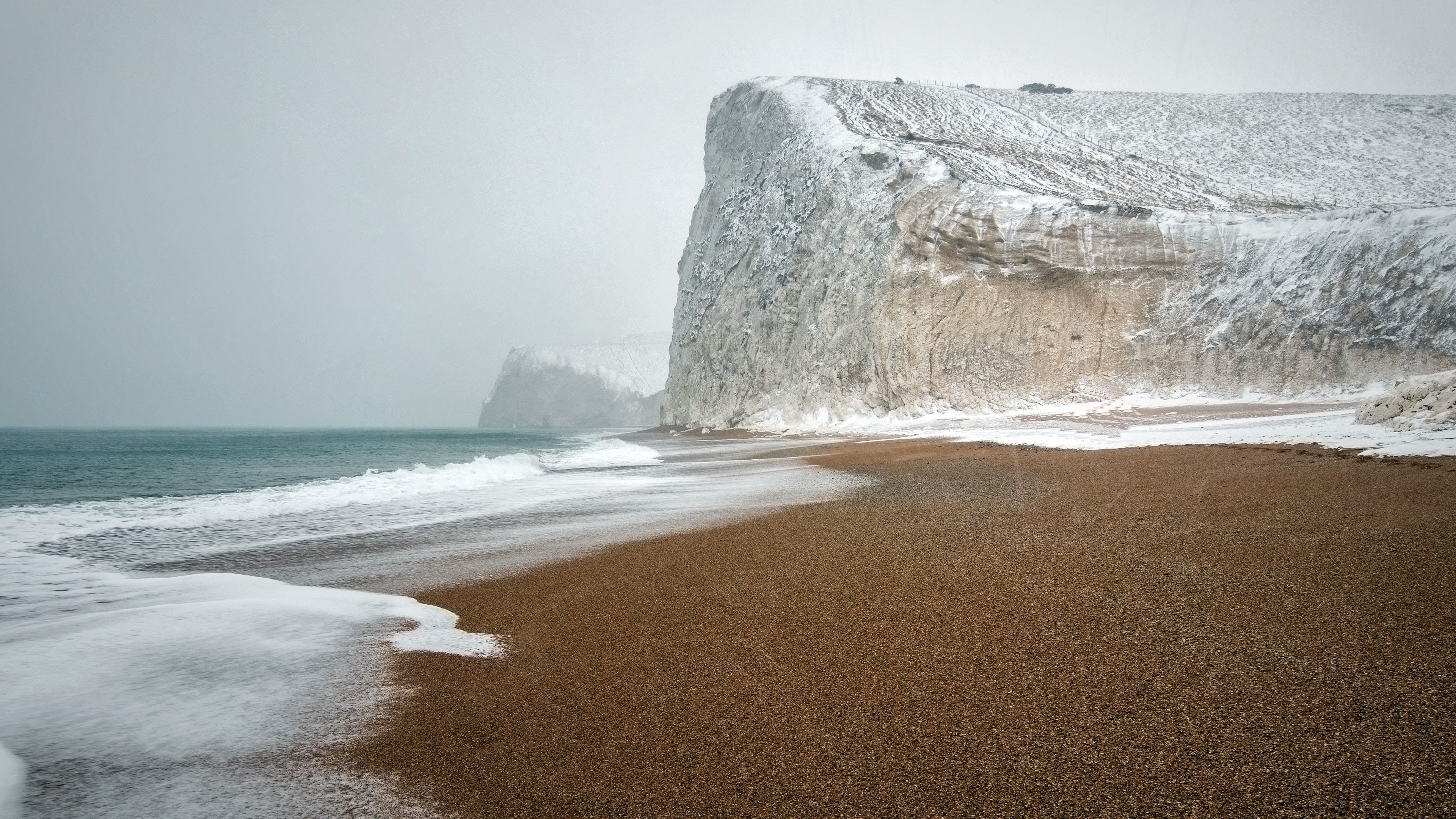 Snow covered cliffs on a beach with ocean waves HD Wallpaper