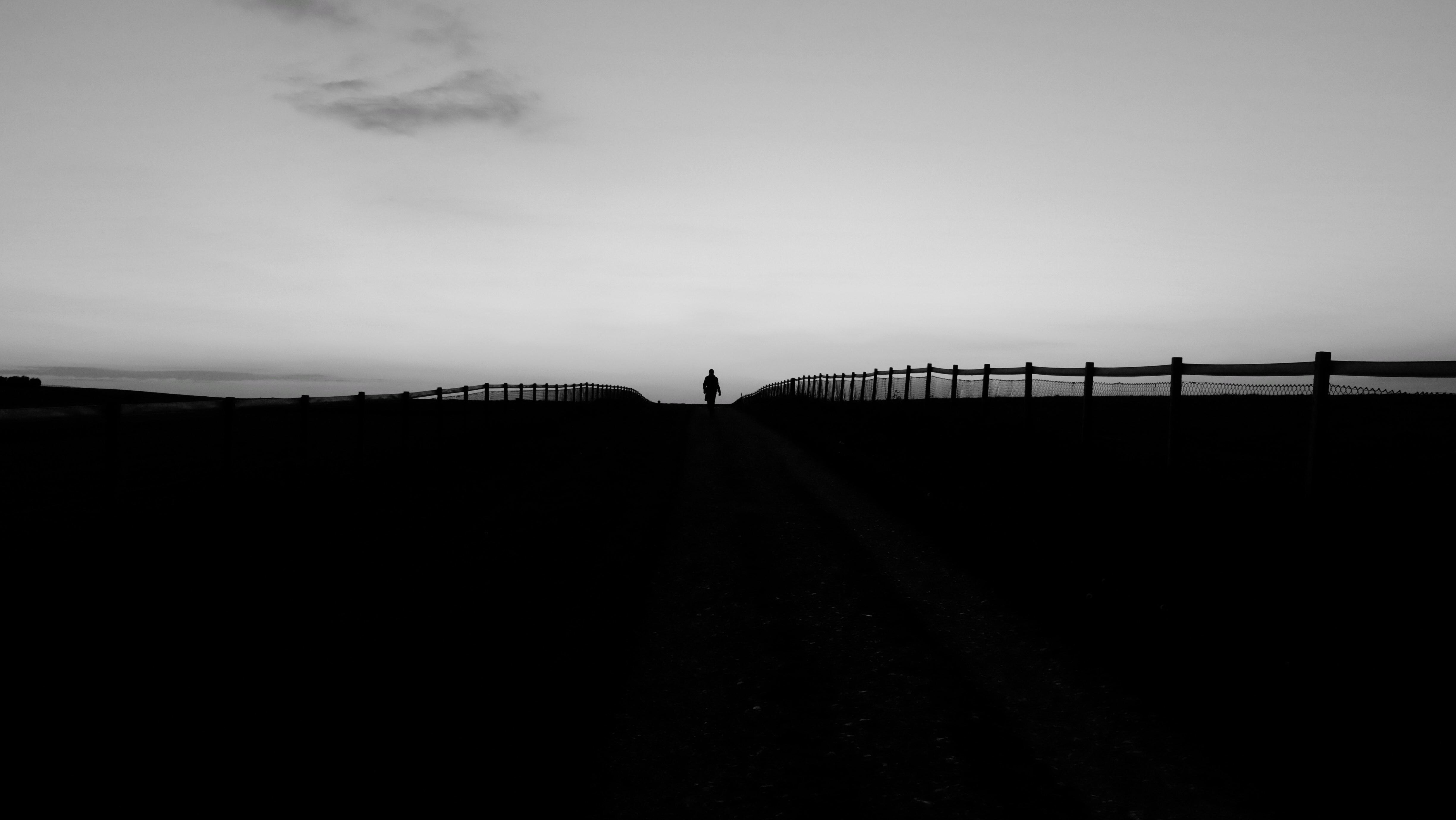 Silhouette of a person walking on a path with fences HD Wallpaper