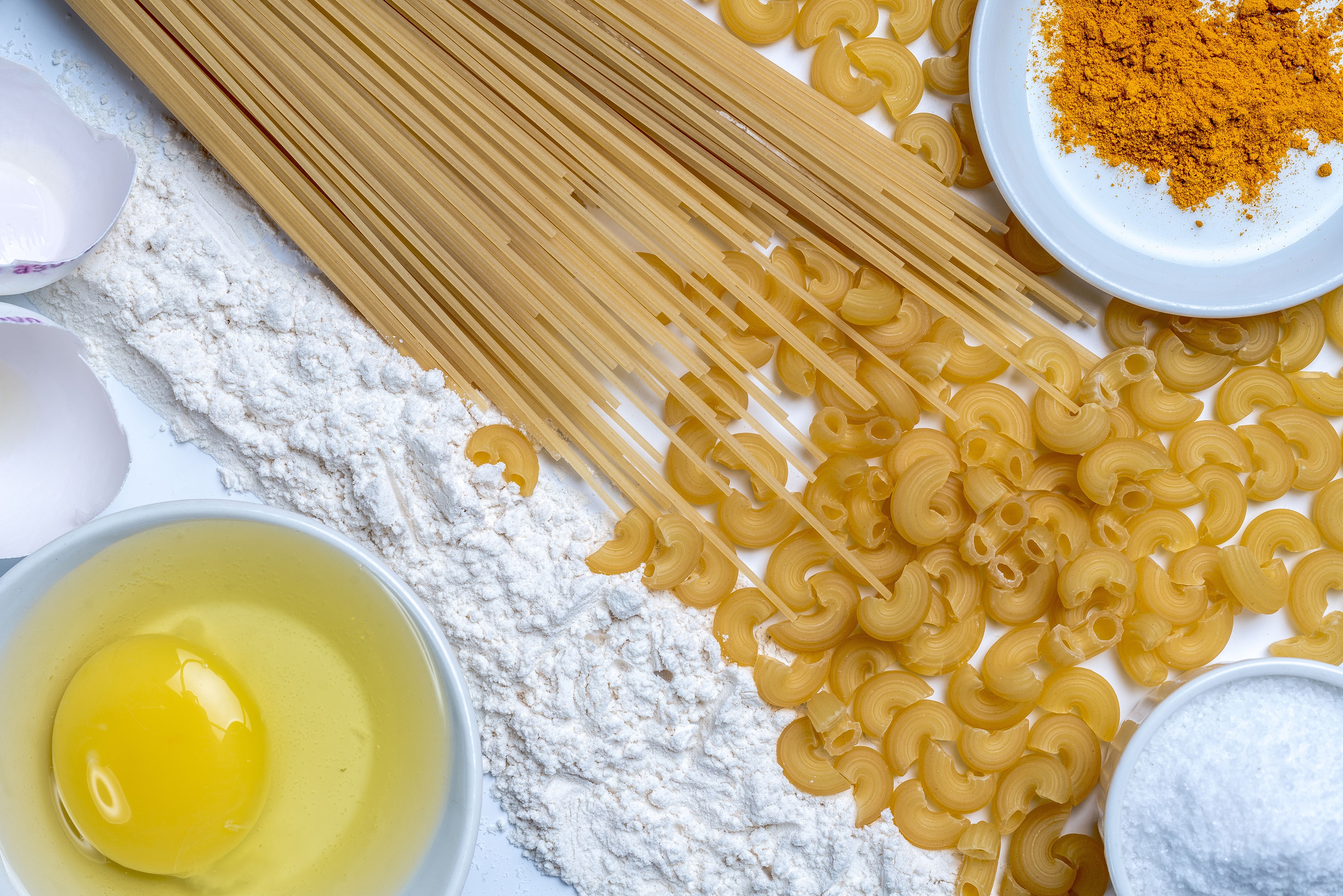 Top view of pasta ingredients: spaghetti, macaroni, flour, egg, and spices HD Wallpaper