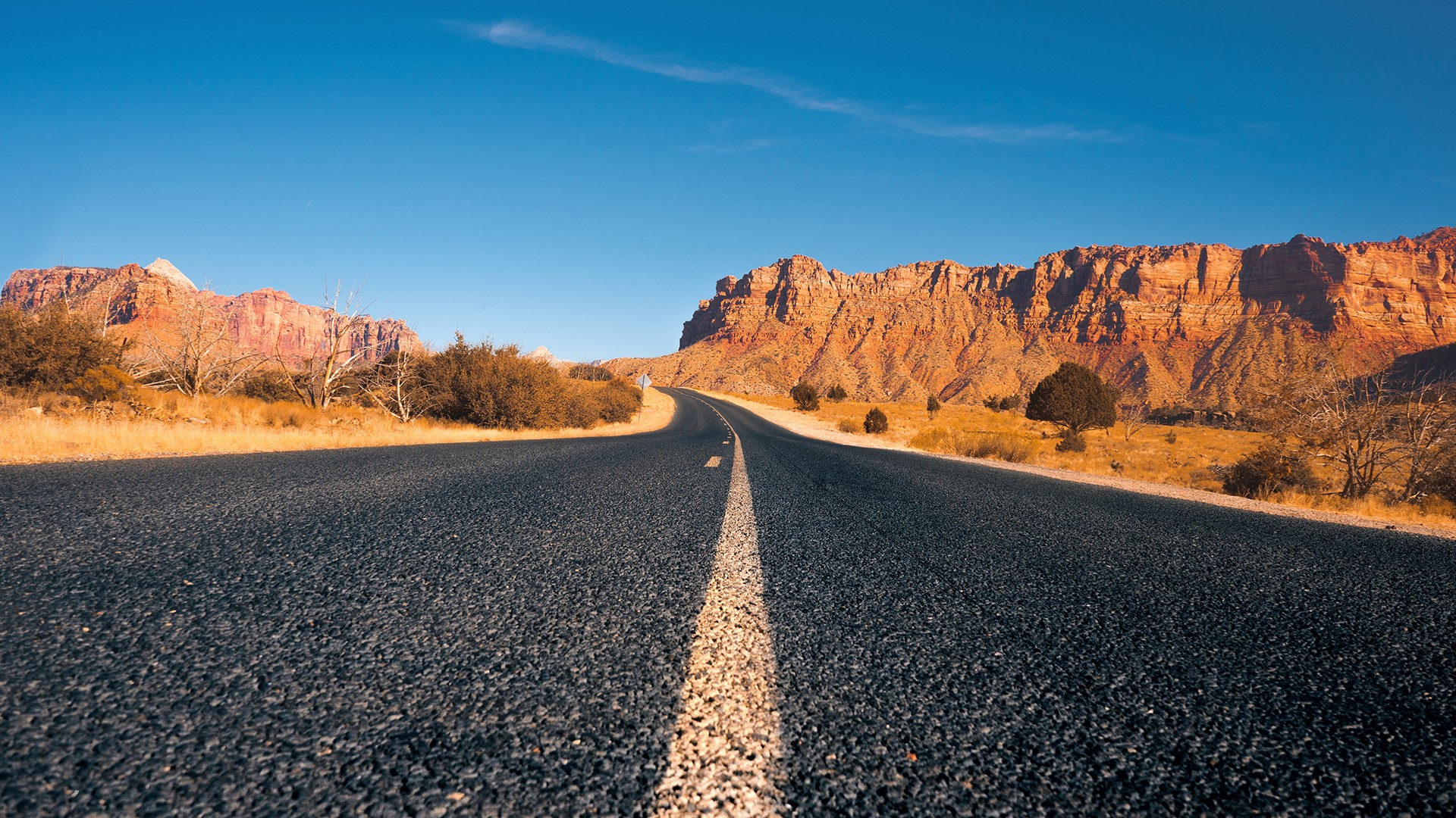 Desert road leading to red rock mountains HD Wallpaper