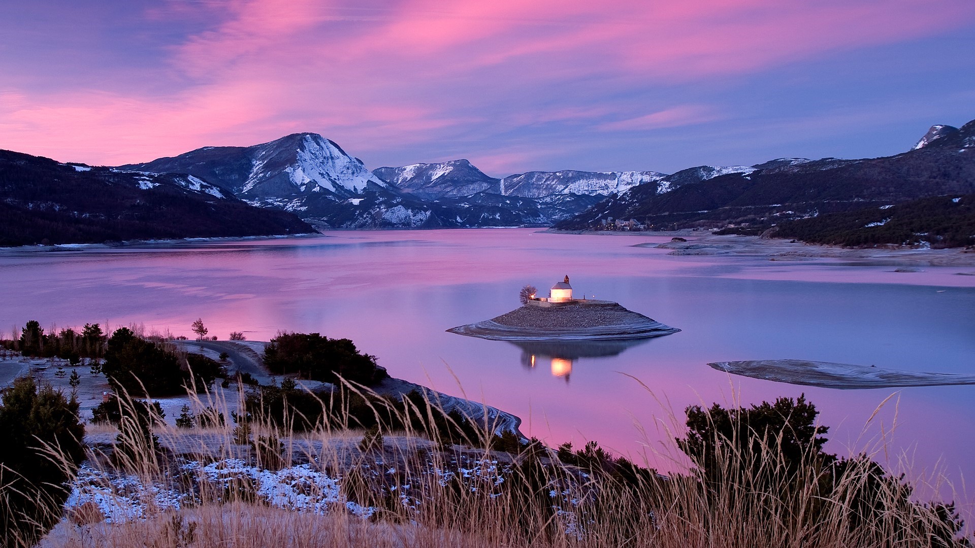Chapel on an island in a lake with snowy mountains and pink sky HD Wallpaper