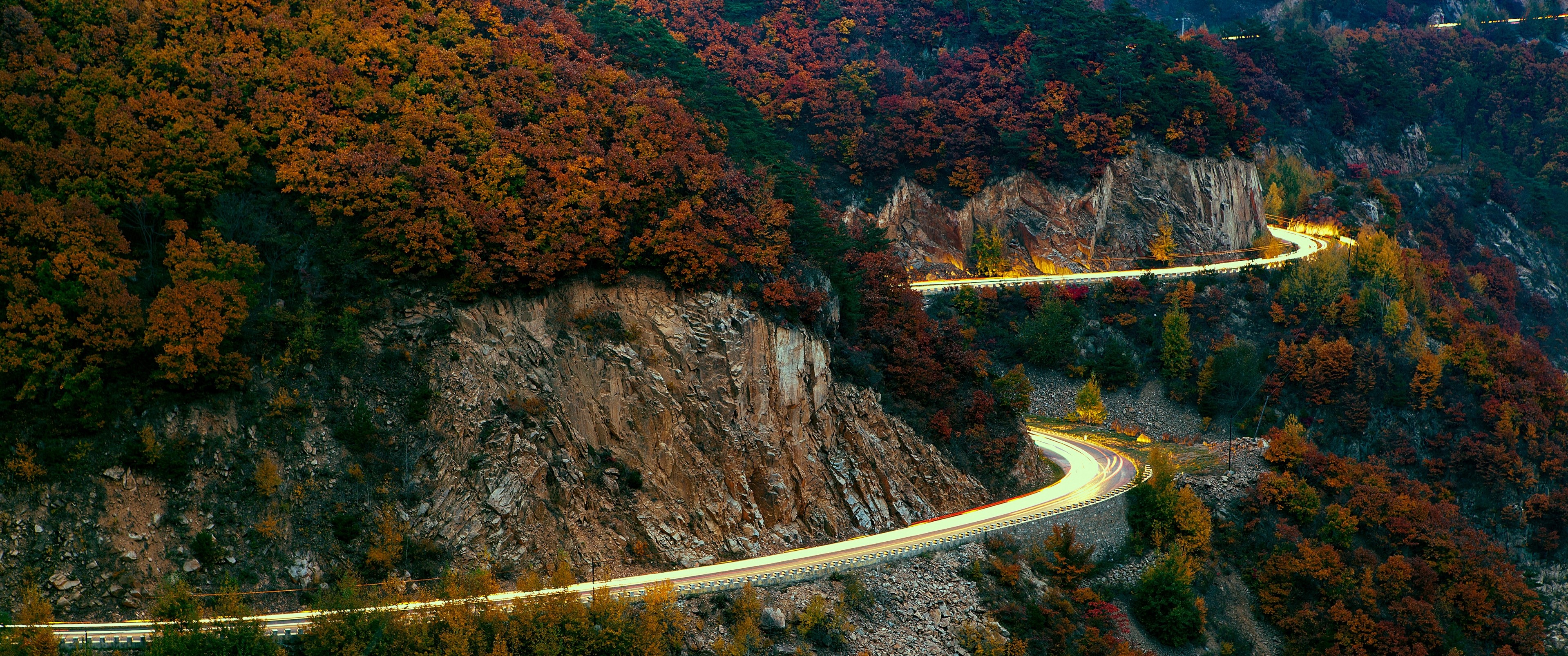 Winding mountain road with autumn foliage and light trails HD Wallpaper