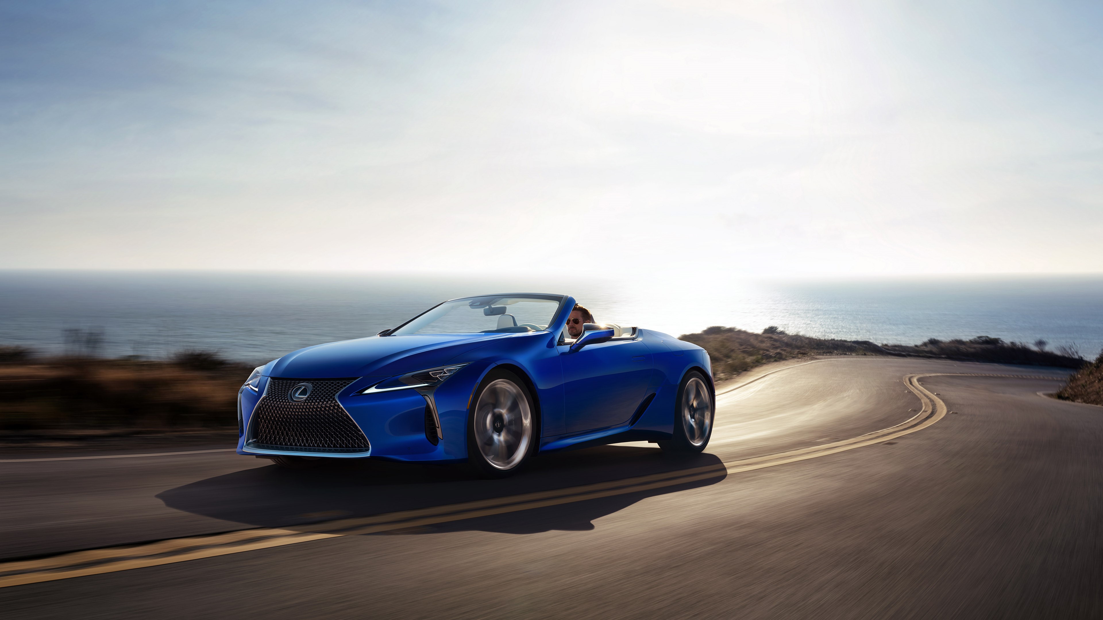 Blue Lexus LC-500 Convertible driving on coastal road at sunset HD Wallpaper