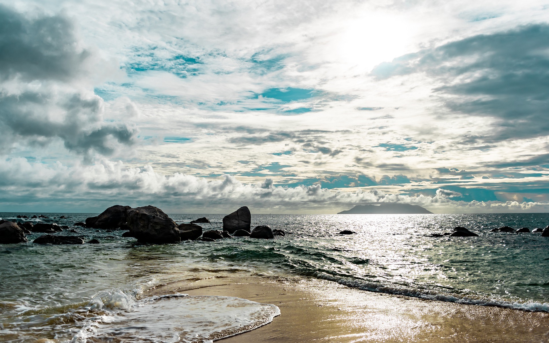 Ocean waves crash on a rocky beach with a distant island HD Wallpaper