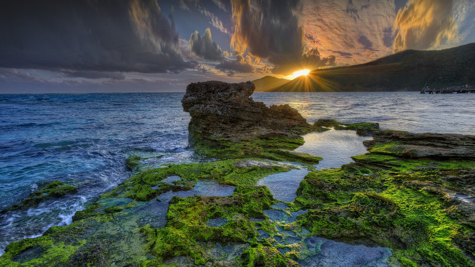 Sunset over the ocean with rocky shore and mountains HD Wallpaper
