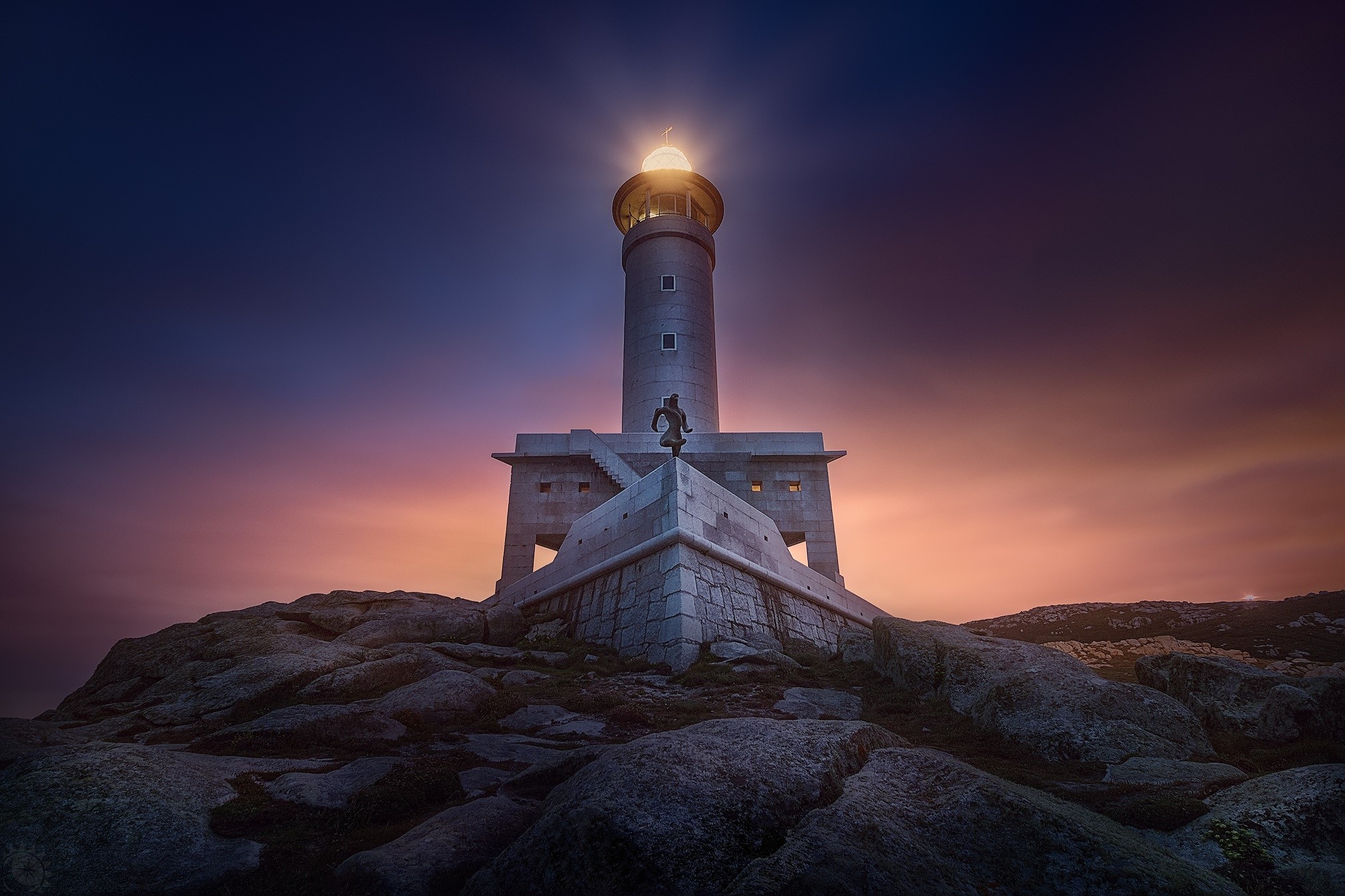Lighthouse on a rocky coast at sunset HD Wallpaper