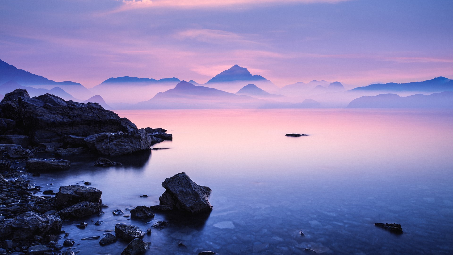 Misty mountains over a calm lake at dawn HD Wallpaper