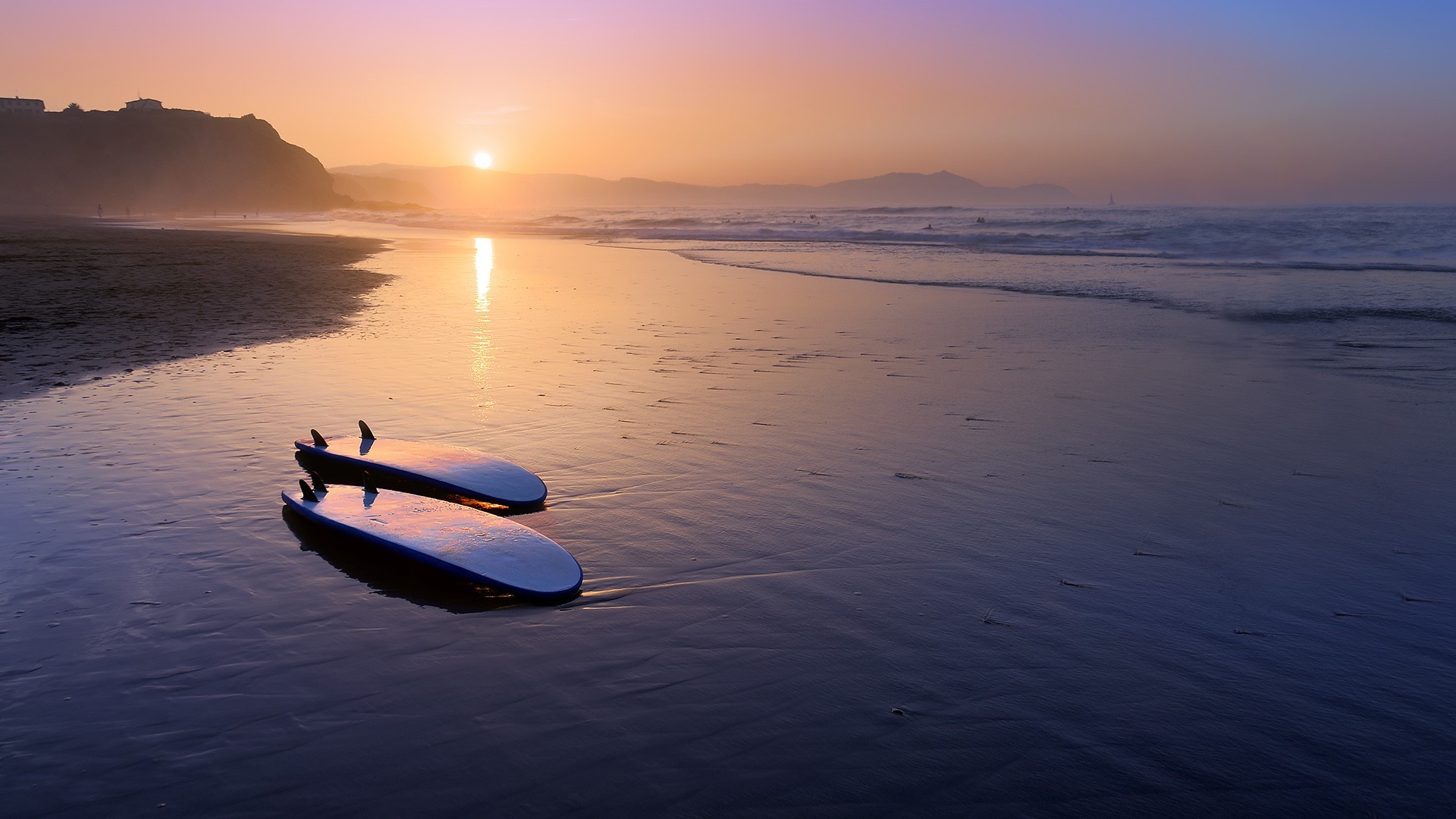 Surfboards on a beach at sunset with mountains HD Wallpaper