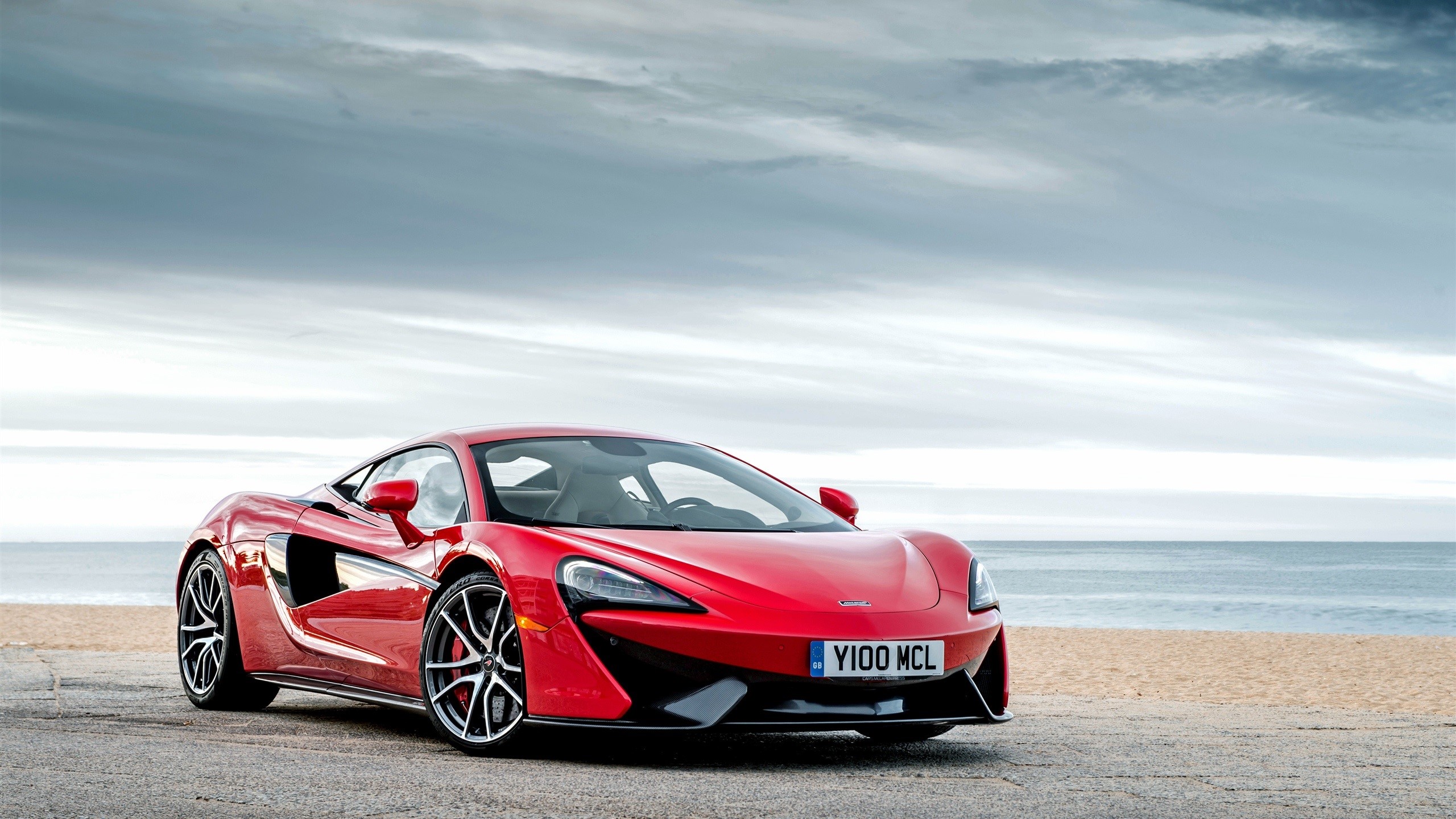 Red McLaren supercar on a beach with clouds HD Wallpaper
