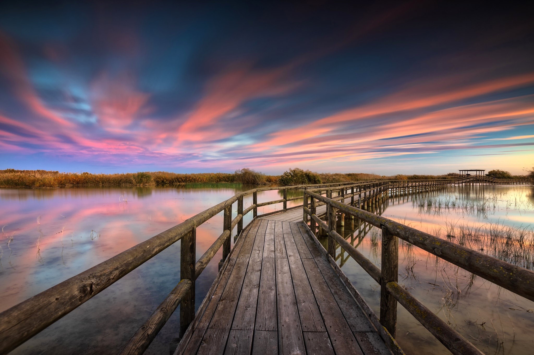 Wooden walkway over water at sunset with colorful clouds HD Wallpaper