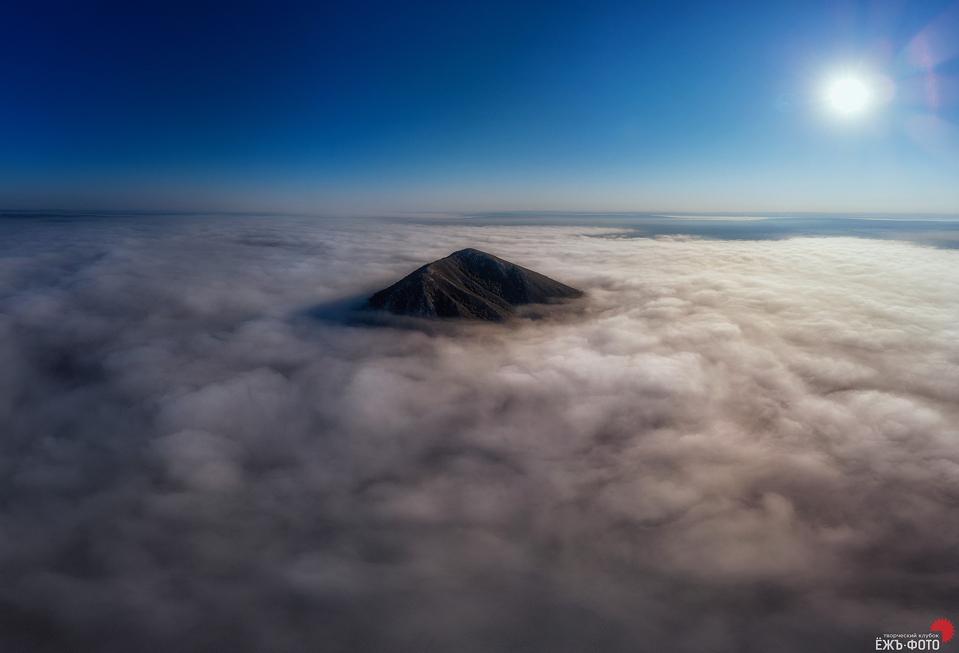 Mountain peak emerging from clouds under a bright sun HD Wallpaper