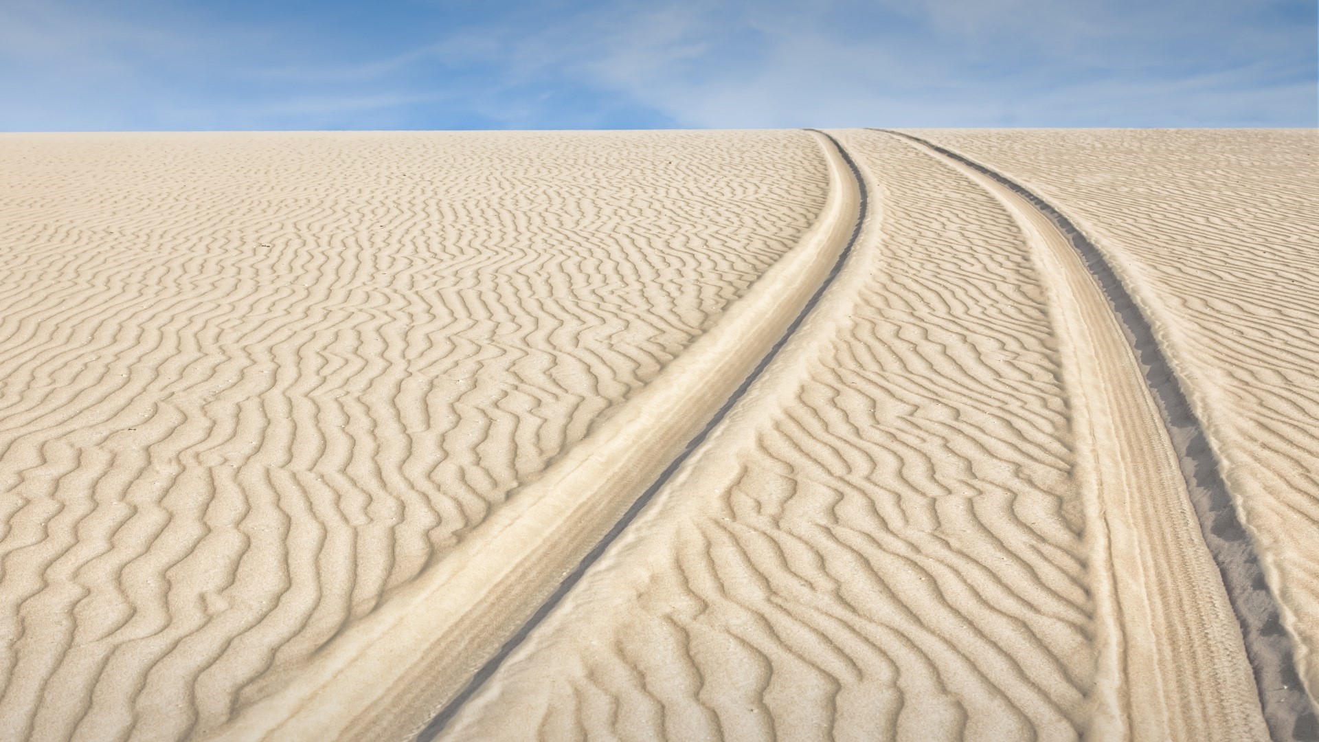 Tire tracks on sand dunes under a blue sky HD Wallpaper