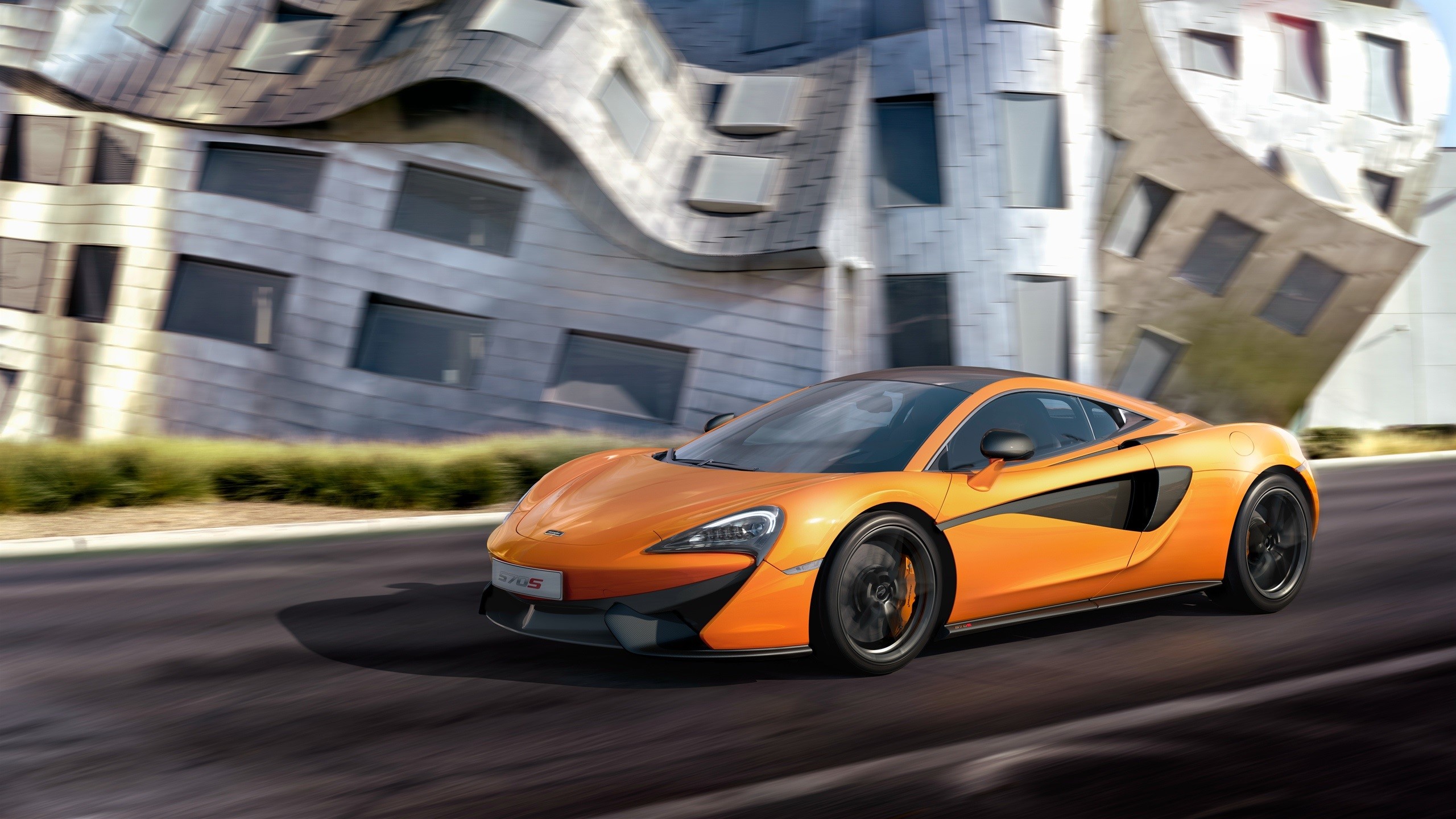Orange McLaren 570S driving on asphalt road HD Wallpaper