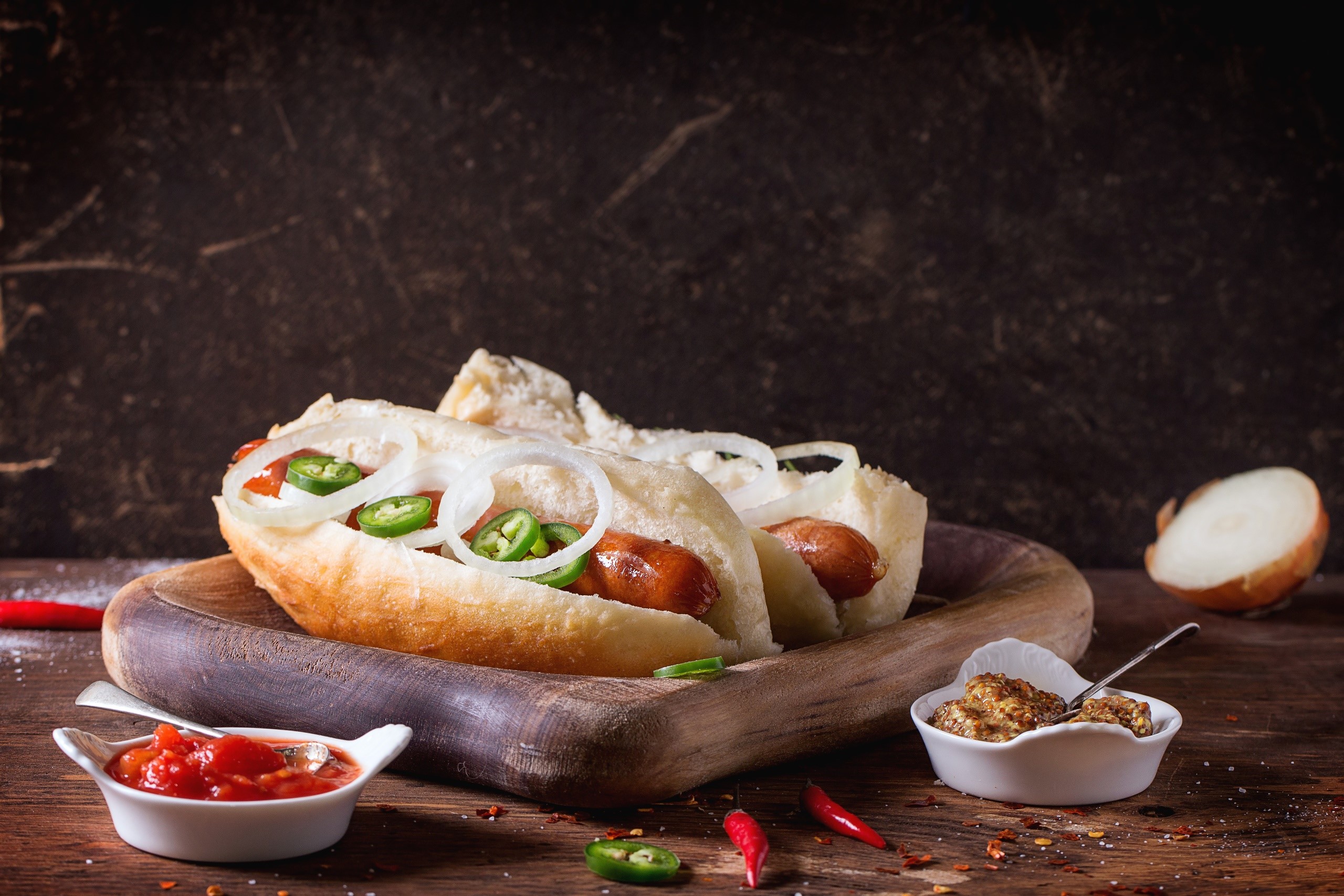Two hot dogs with onions and jalapenos on a wooden board HD Wallpaper