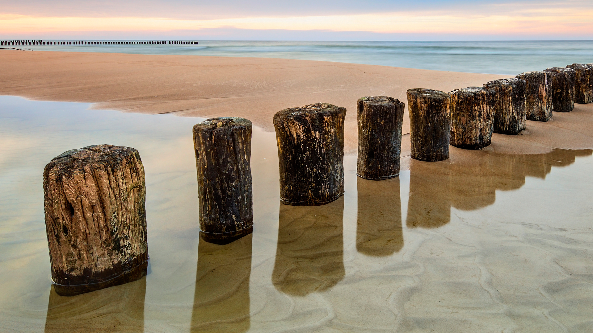 Wooden breakwaters on a sandy beach at sunrise HD Wallpaper