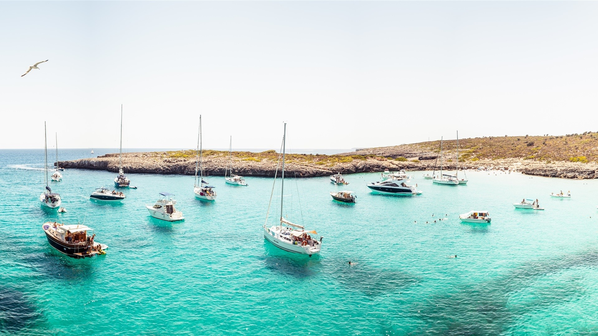 Boats anchored in a clear turquoise bay with rocky shores HD Wallpaper