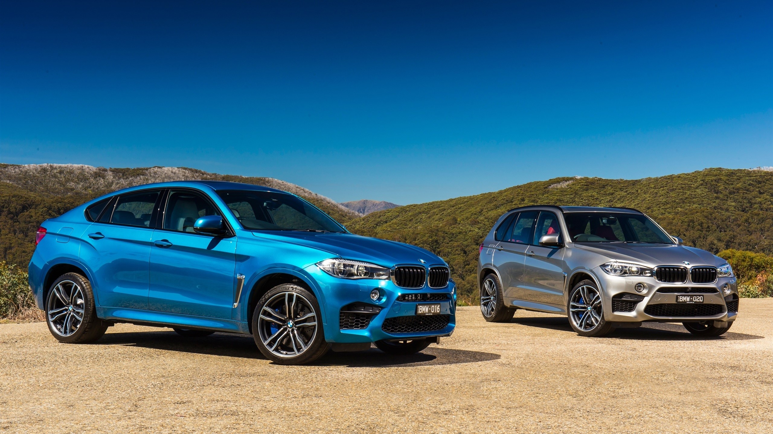 Two BMW SUVs parked outdoors with mountains in background HD Wallpaper