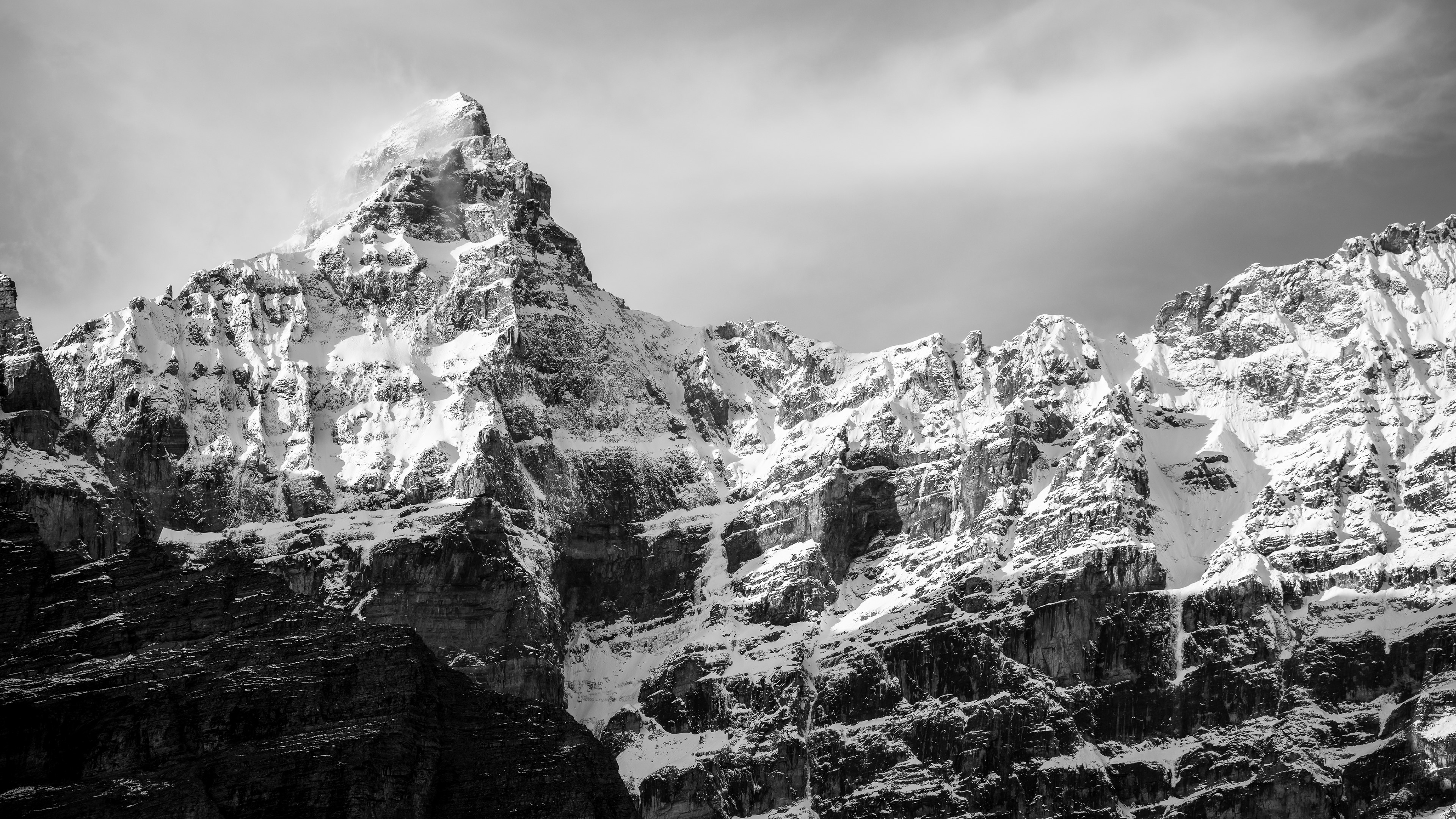 Snow-covered rocky mountains under a cloudy sky HD Wallpaper