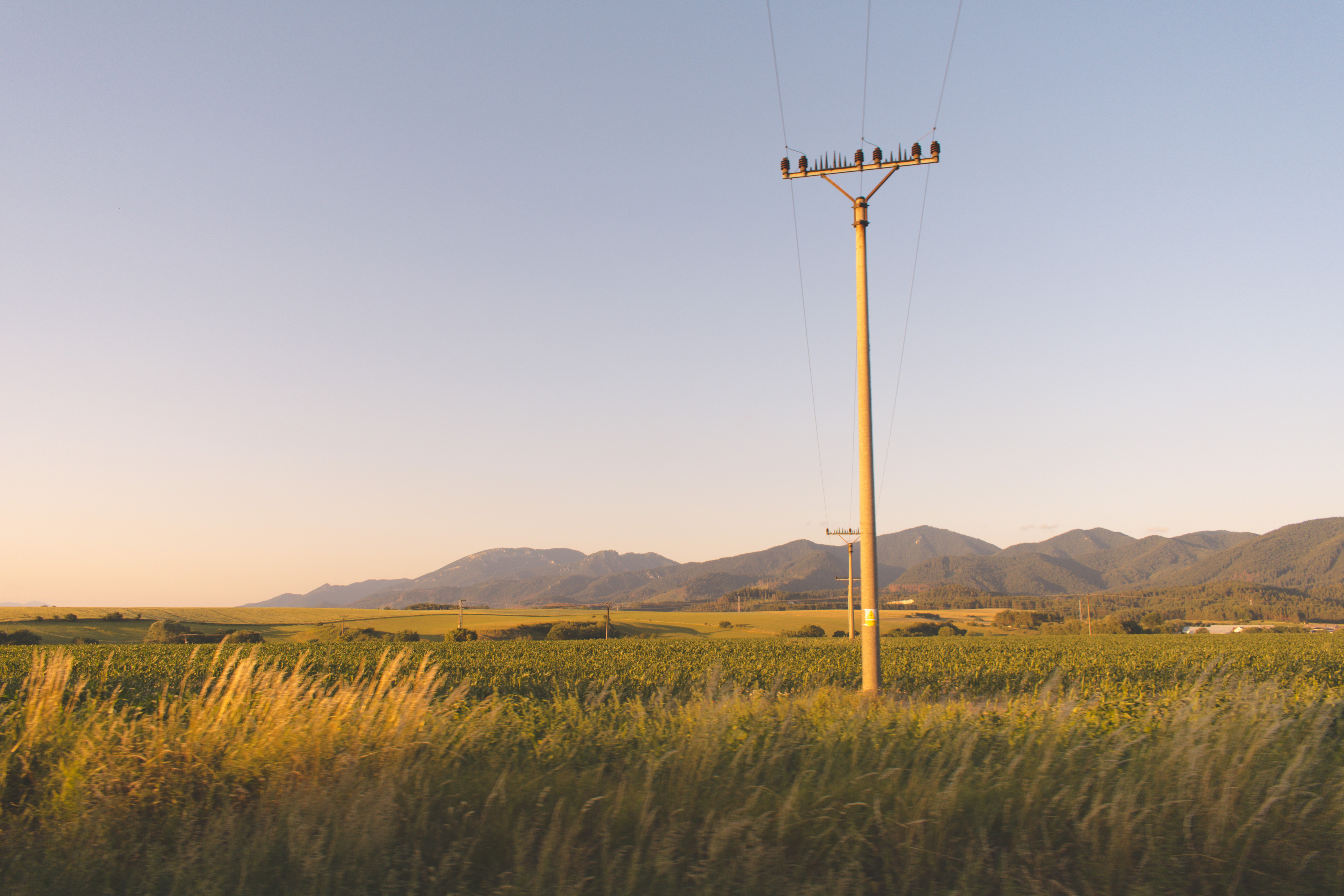 Power lines in a field with mountains at sunset HD Wallpaper