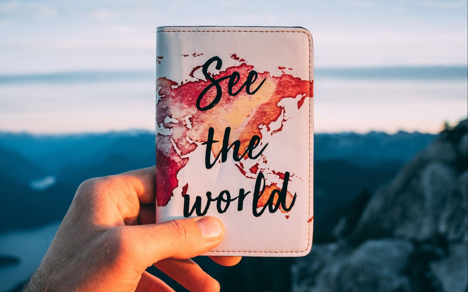 Hand holding a passport cover with a world map HD Wallpaper