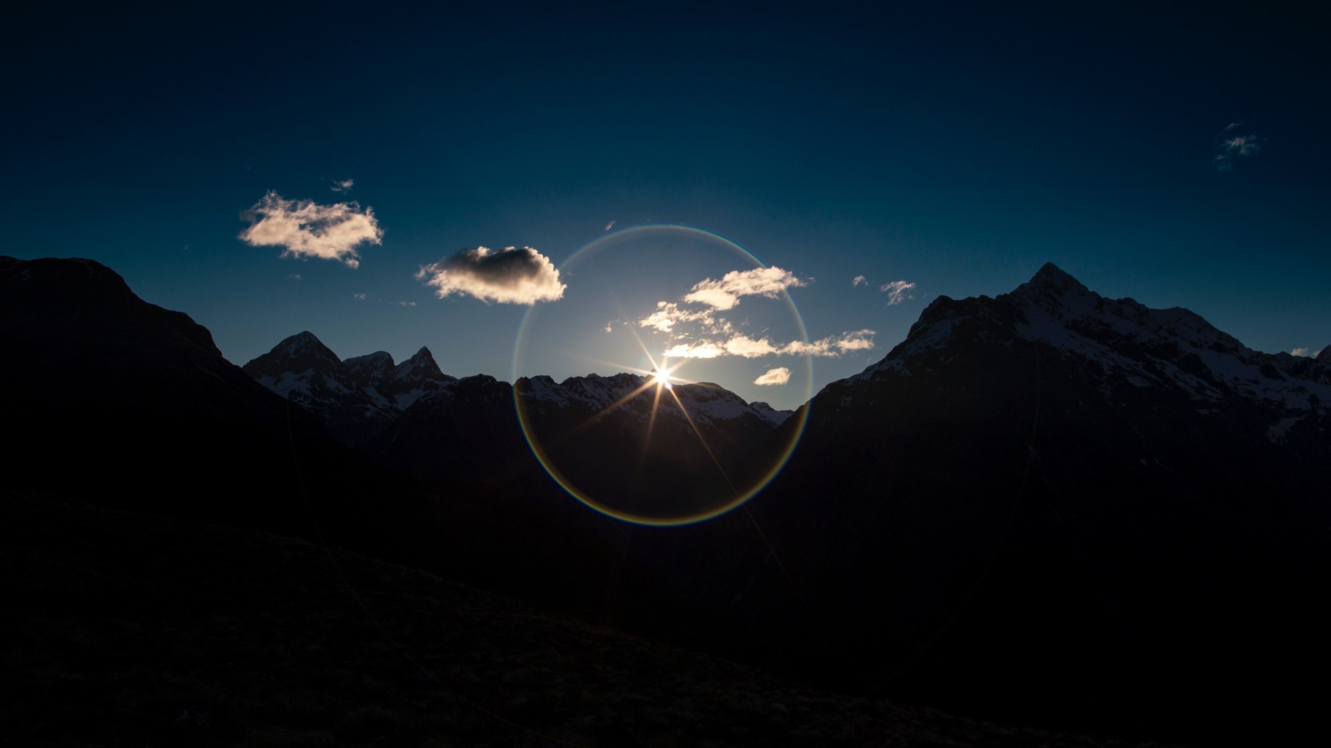 Sun setting behind snow-capped mountains with clouds HD Wallpaper