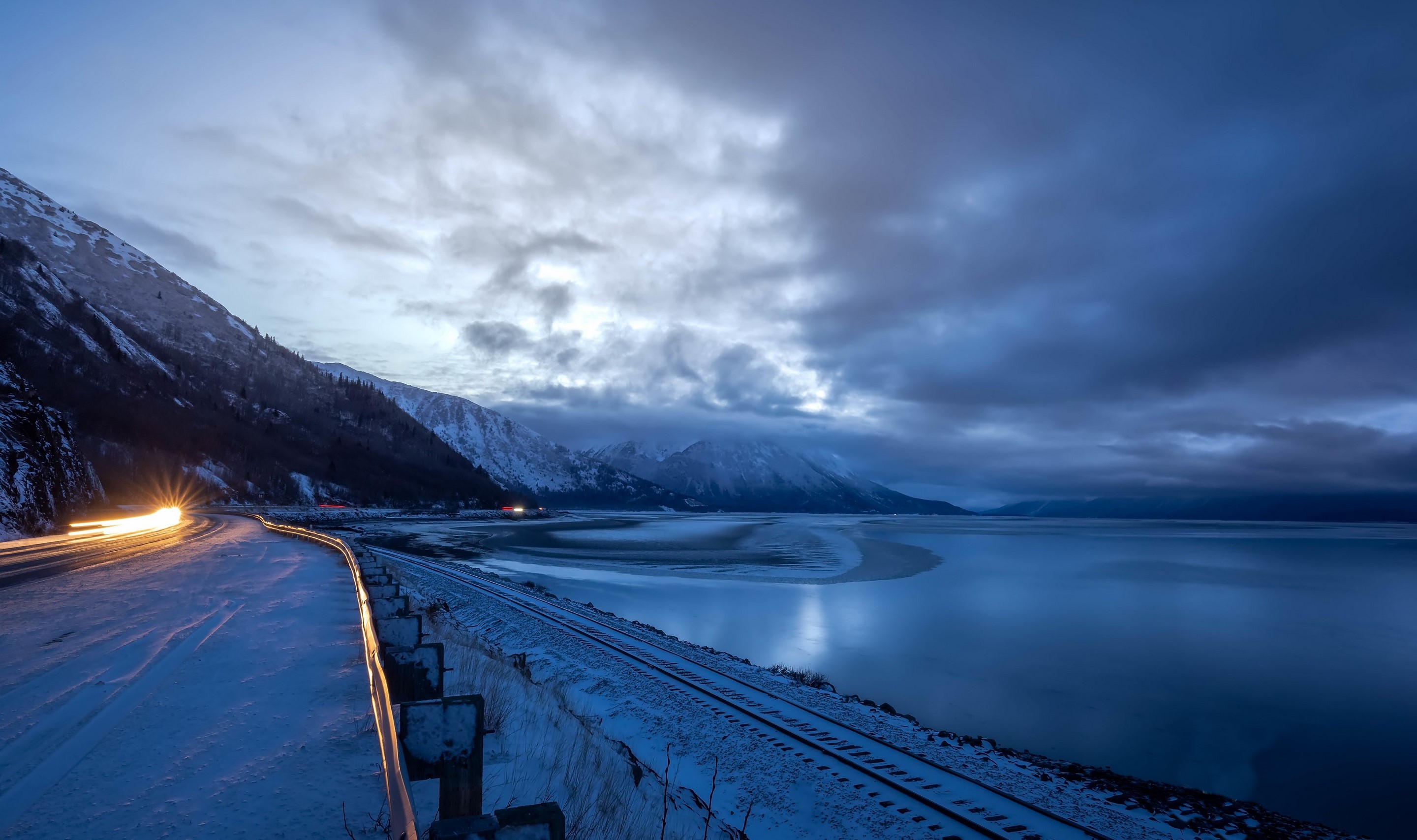 Snowy road and train tracks by a bay at dusk HD Wallpaper