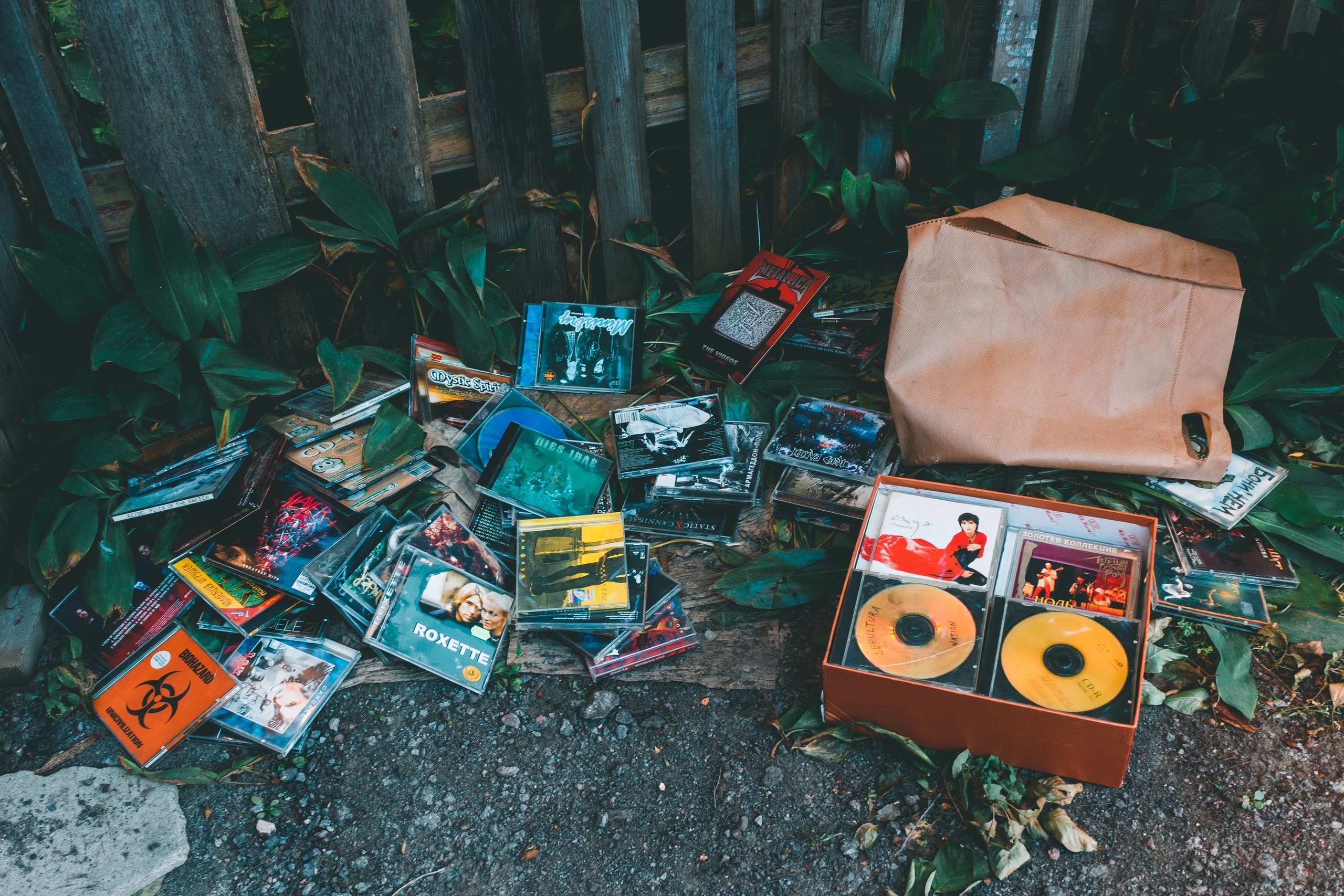 Pile of CDs and a paper bag by a fence HD Wallpaper