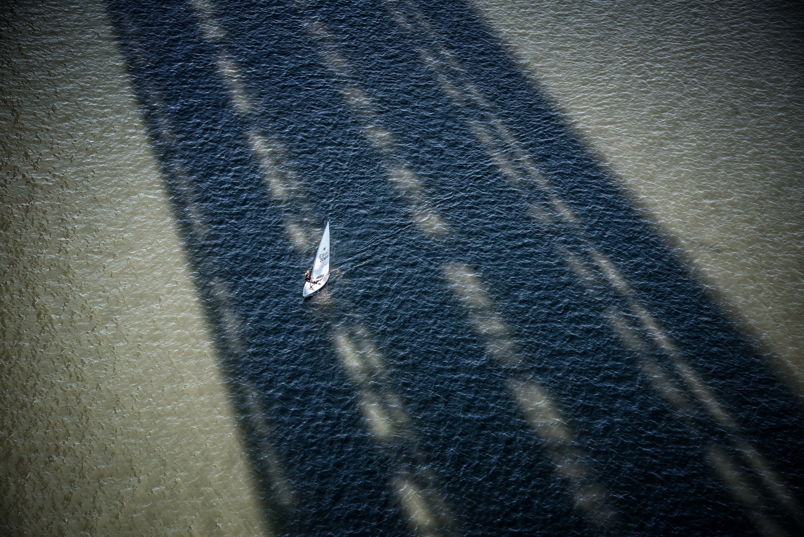 Sailboat under a bridge's shadow on the water HD Wallpaper