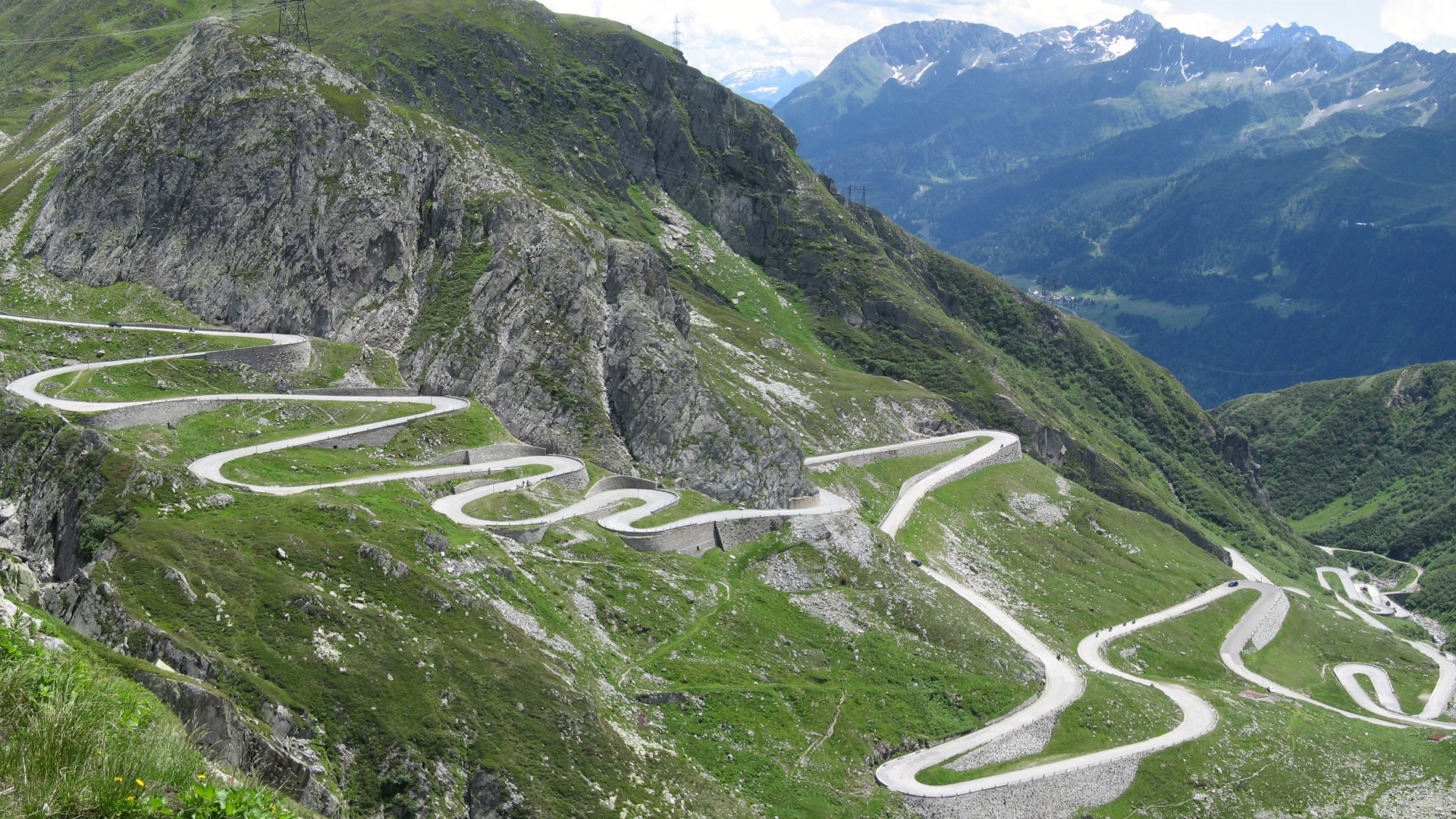 Serpentine mountain road winding through green slopes HD Wallpaper