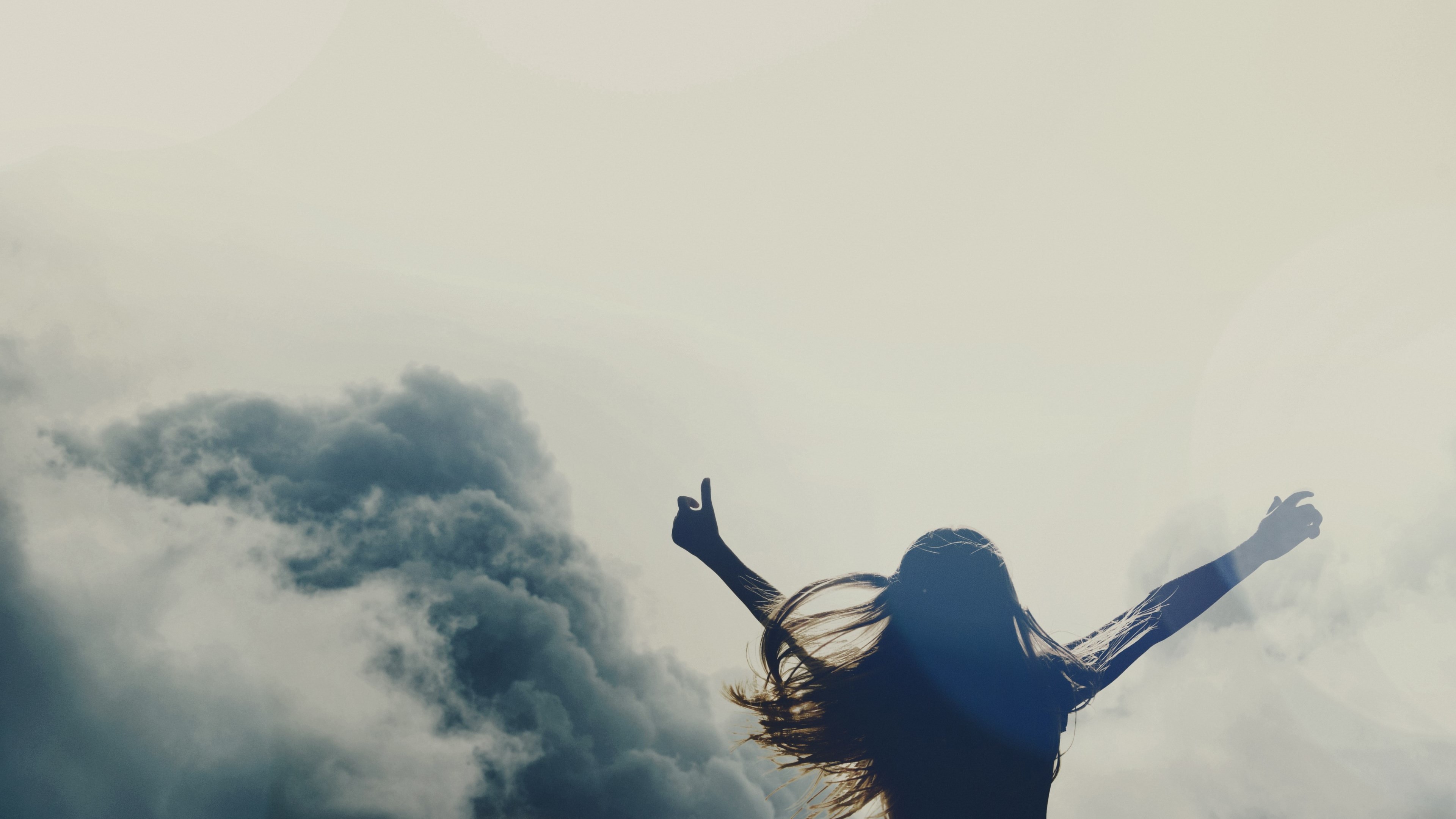 Silhouette of a woman with arms raised against clouds HD Wallpaper