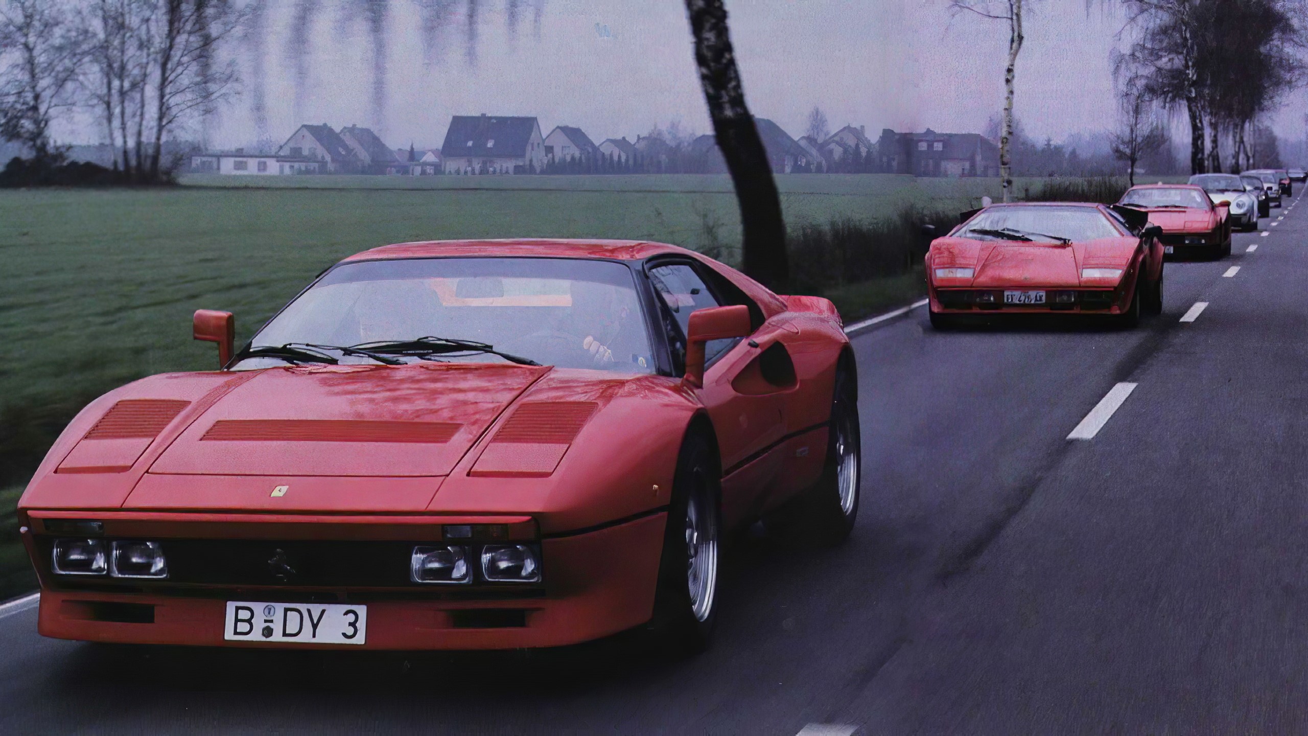 Red Ferraris and Lamborghinis driving on a road HD Wallpaper