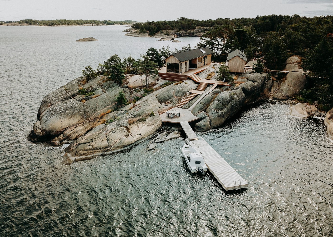 Modern cabin on rocky island with pier and boat HD Wallpaper