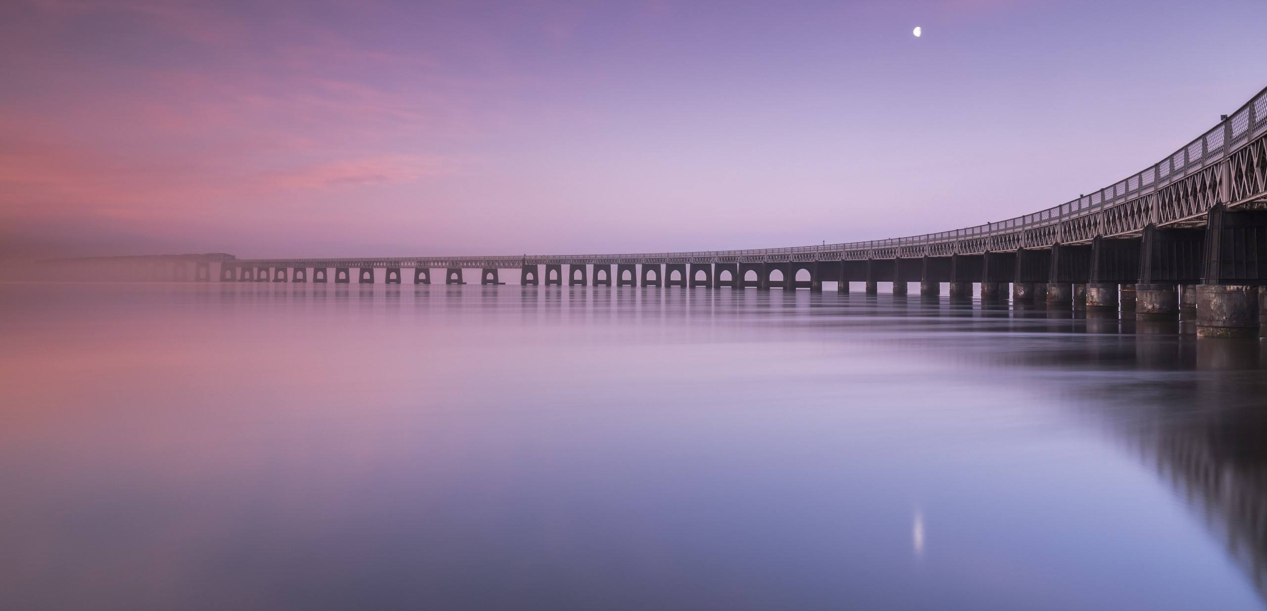 Long bridge over calm water at sunrise with moon HD Wallpaper