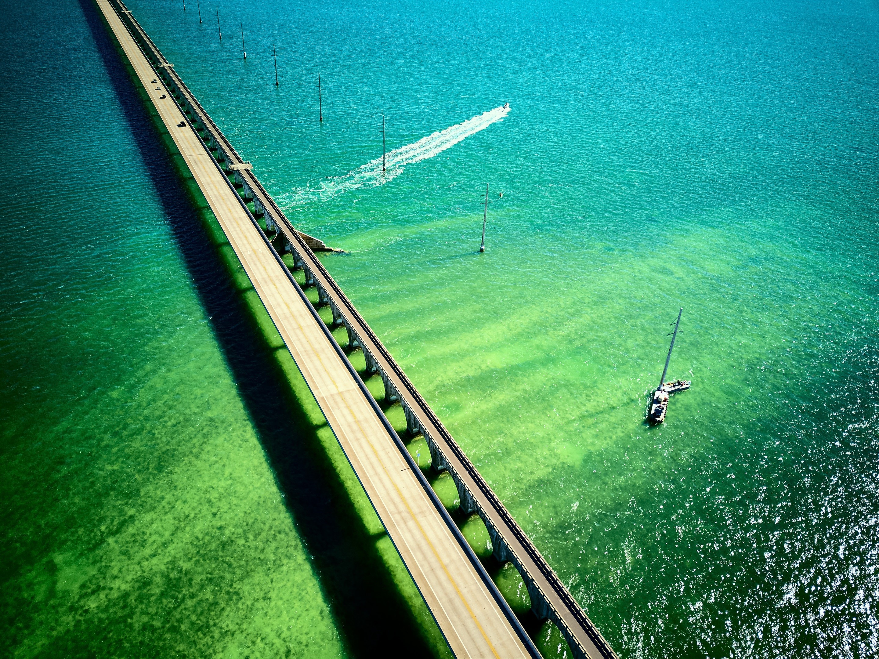 Aerial view of a long bridge over turquoise water with boats HD Wallpaper