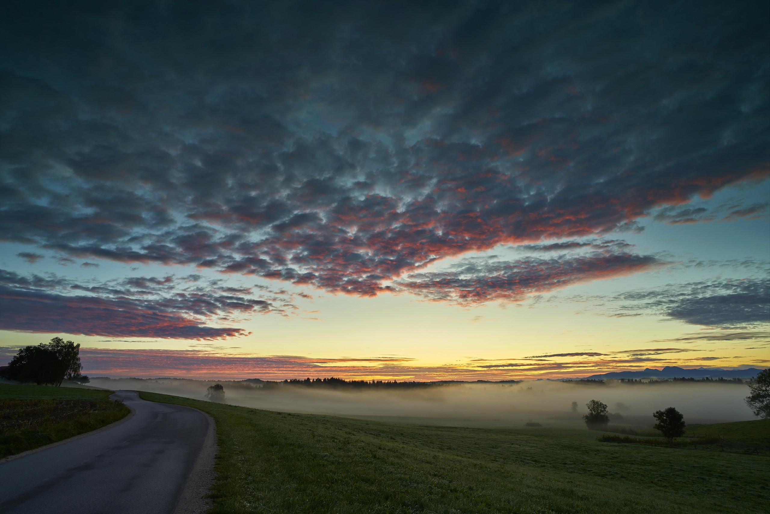 Misty sunrise over a rural landscape with a winding road HD Wallpaper