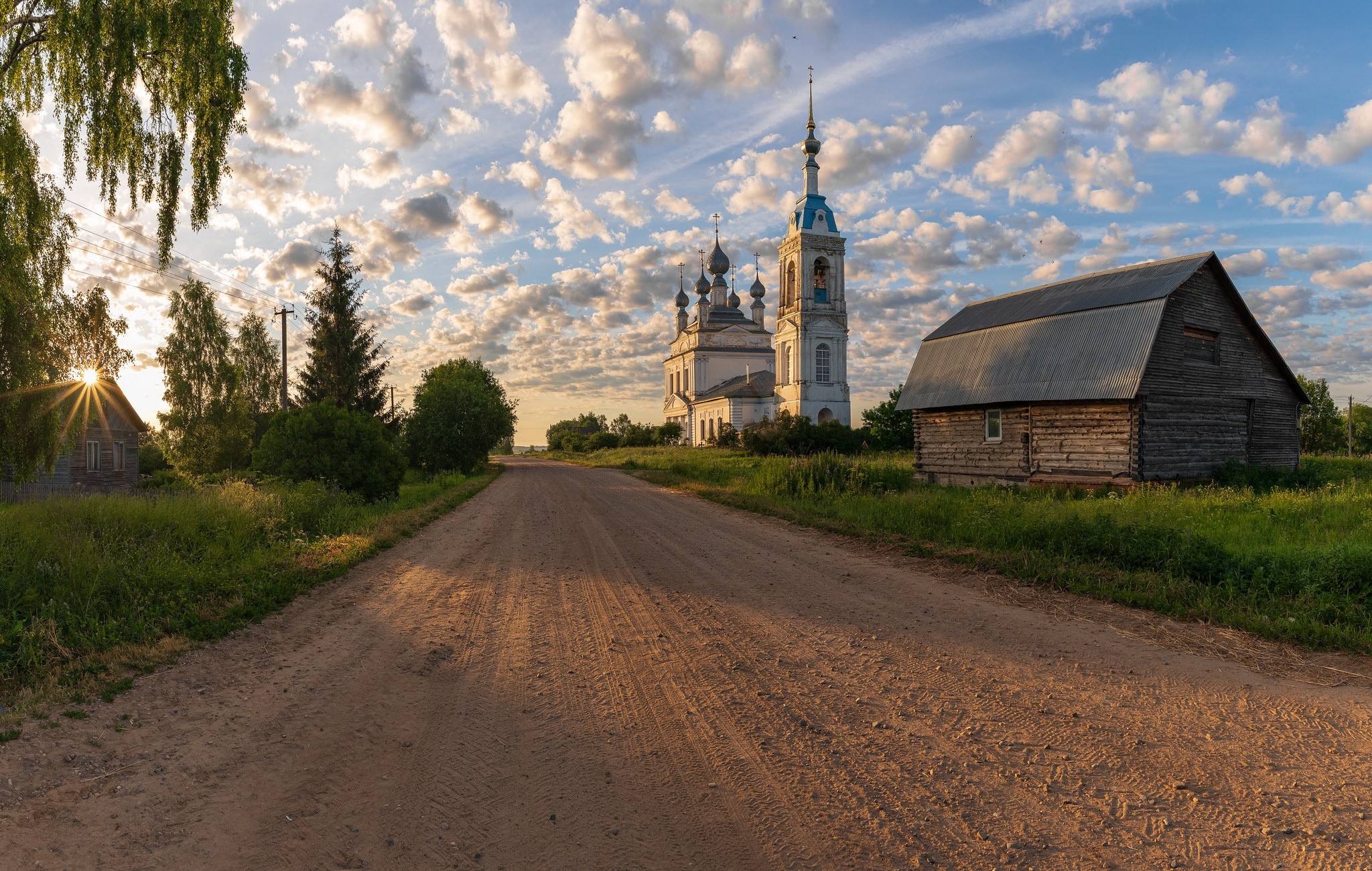 Dirt road leading to a church and barn in a Russian village at sunset HD Wallpaper