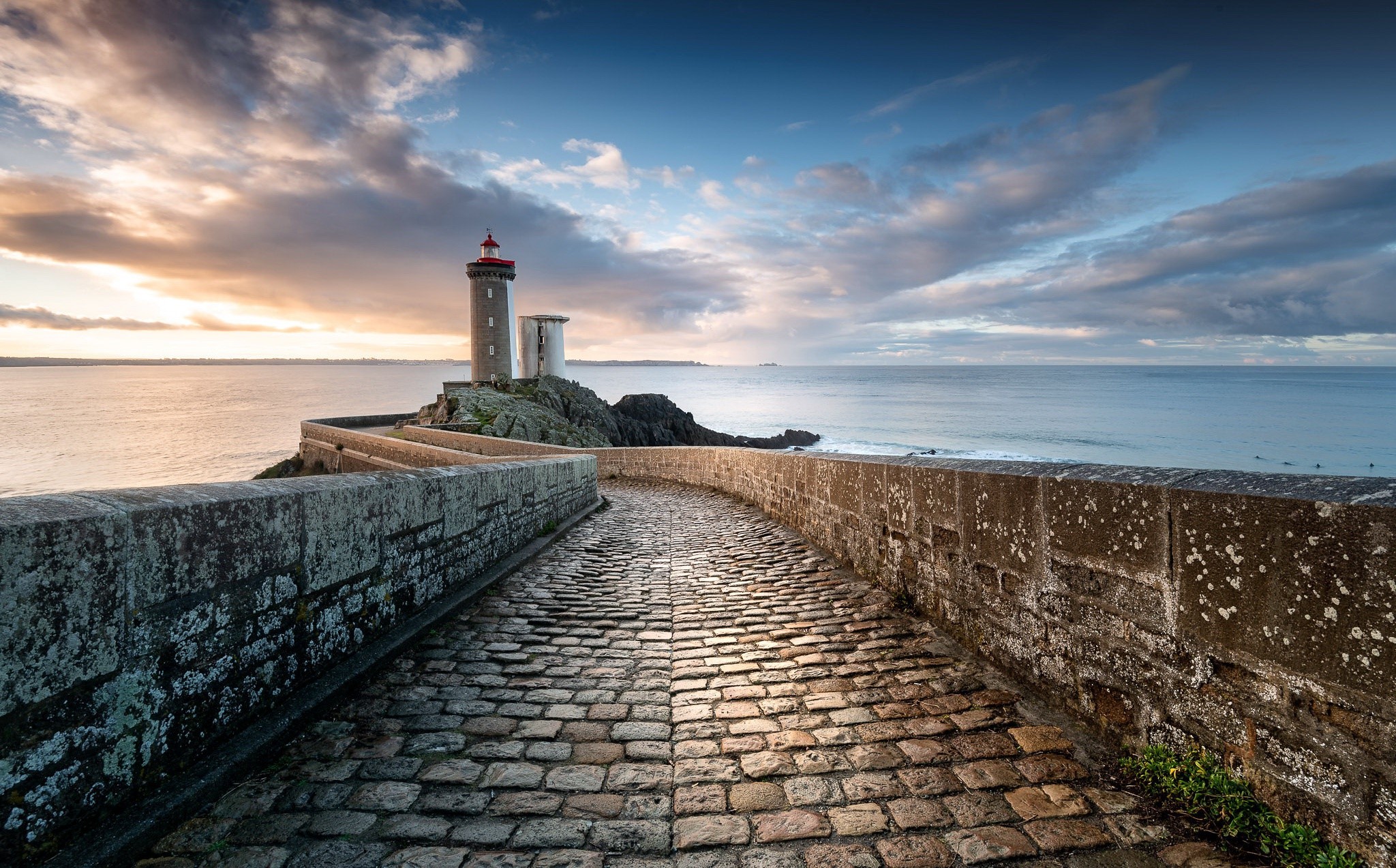 Lighthouse on a rocky outcrop with a cobblestone path HD Wallpaper