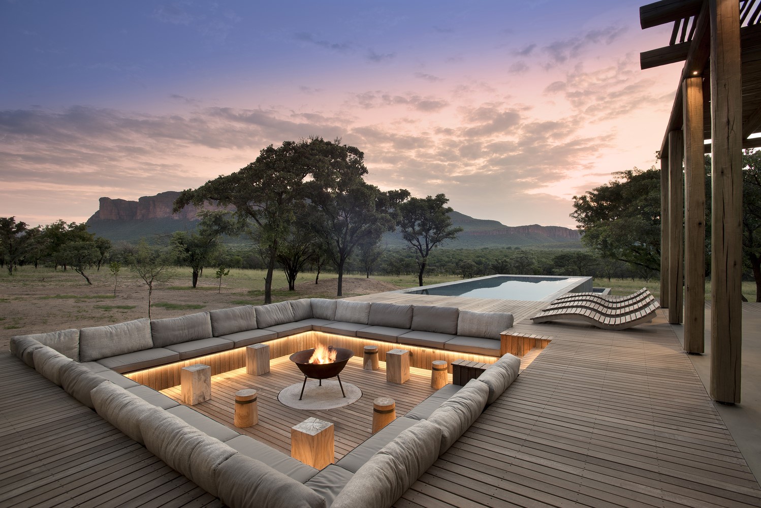 Outdoor lounge area with campfire and swimming pool at sunset HD Wallpaper