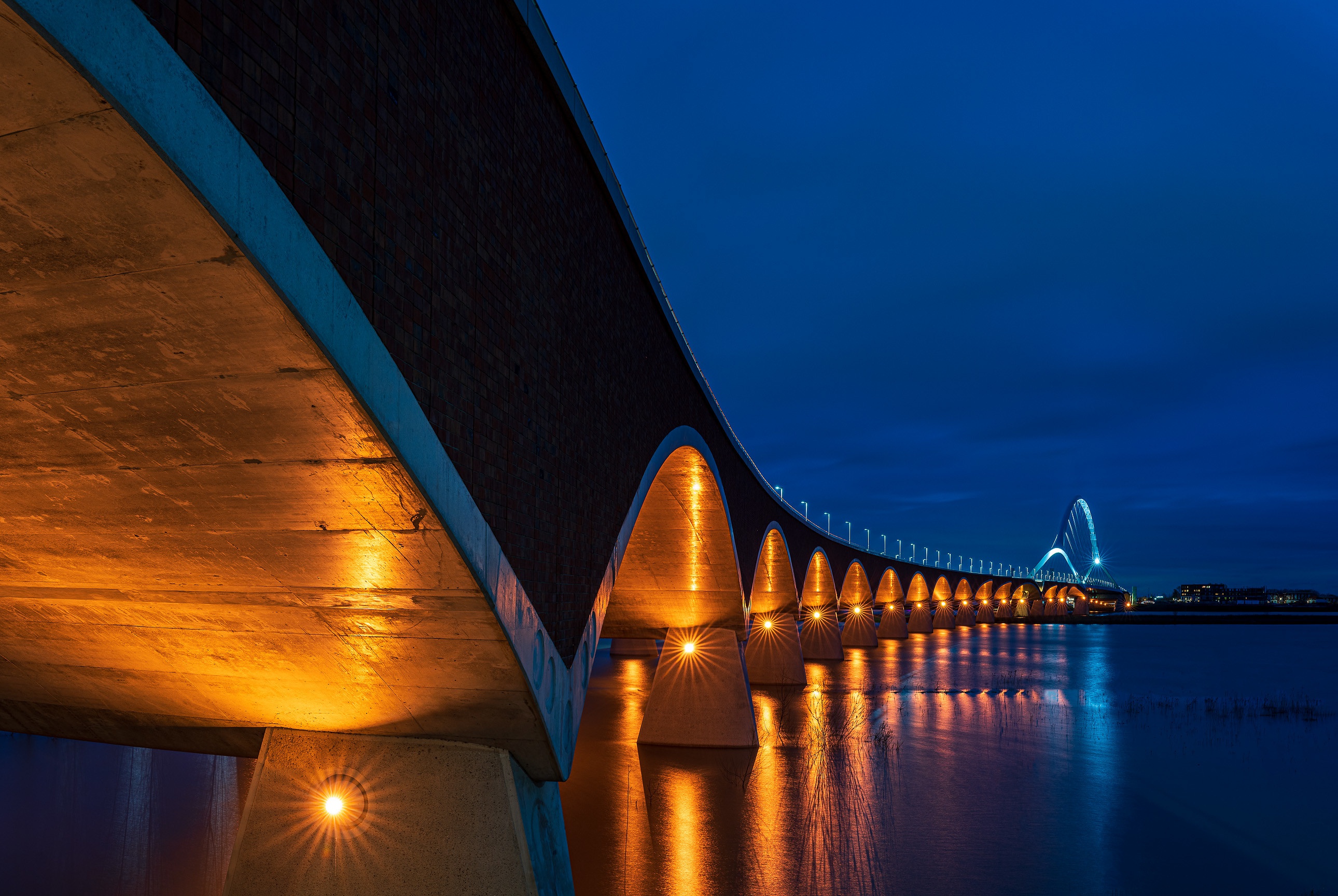Bridge illuminated at night over water HD Wallpaper