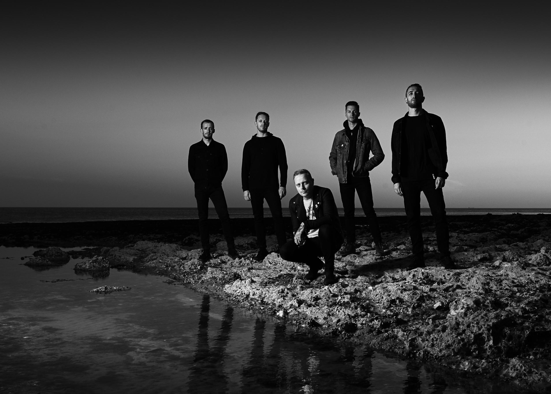 Architects band members on rocky shore at sunset HD Wallpaper